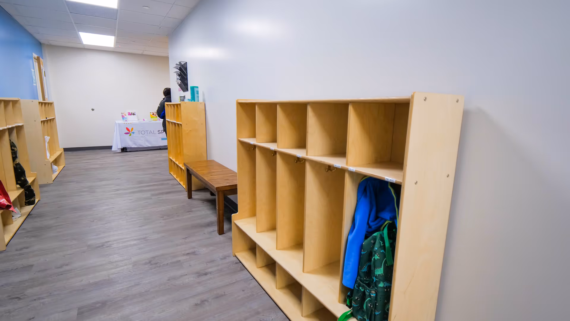 Long hallway with wooden cubbies along the wall, a bench, and a reception table in distance.