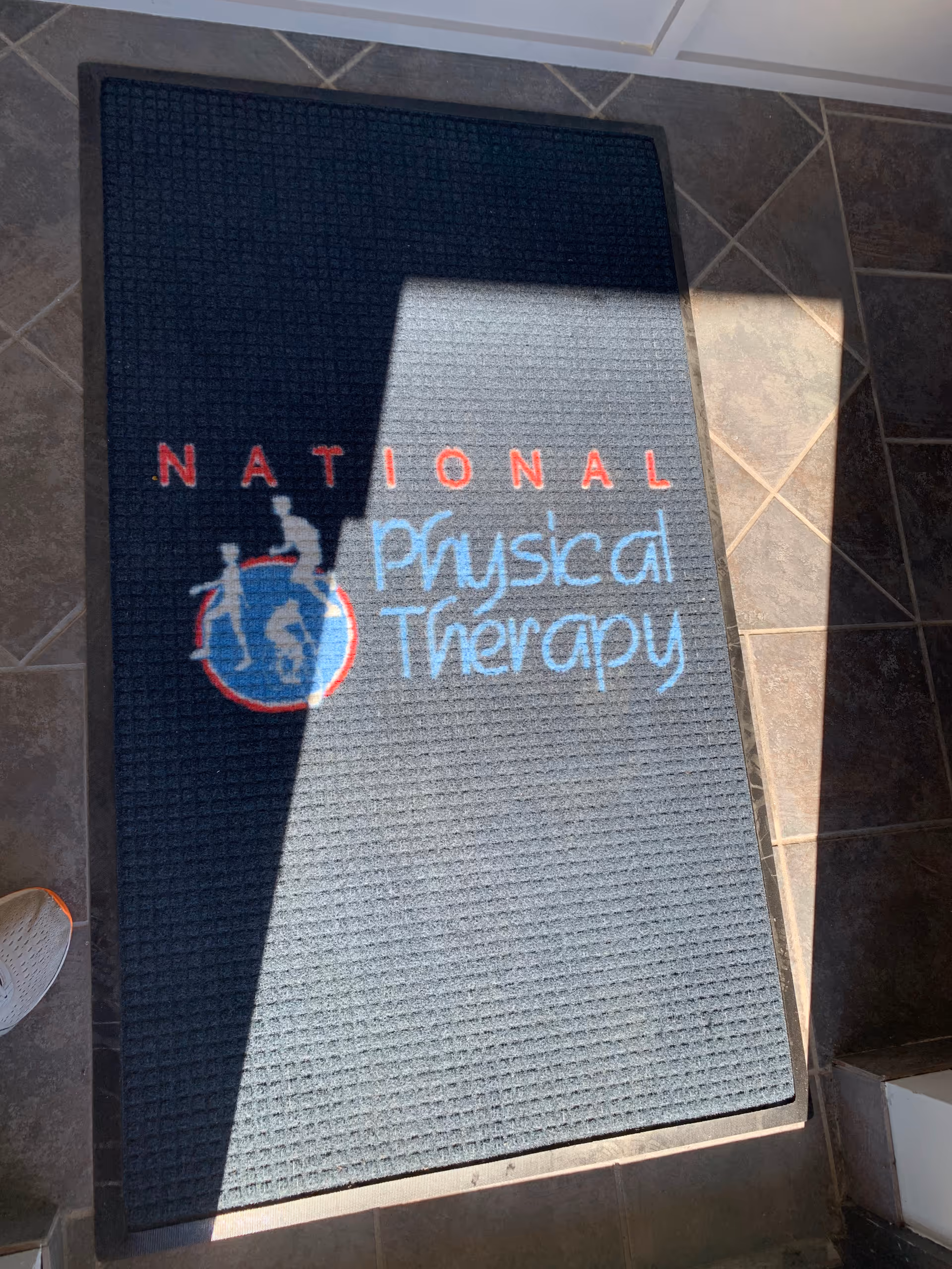 Dark blue entrance mat with National Physical Therapy logo on tiled floor inside.