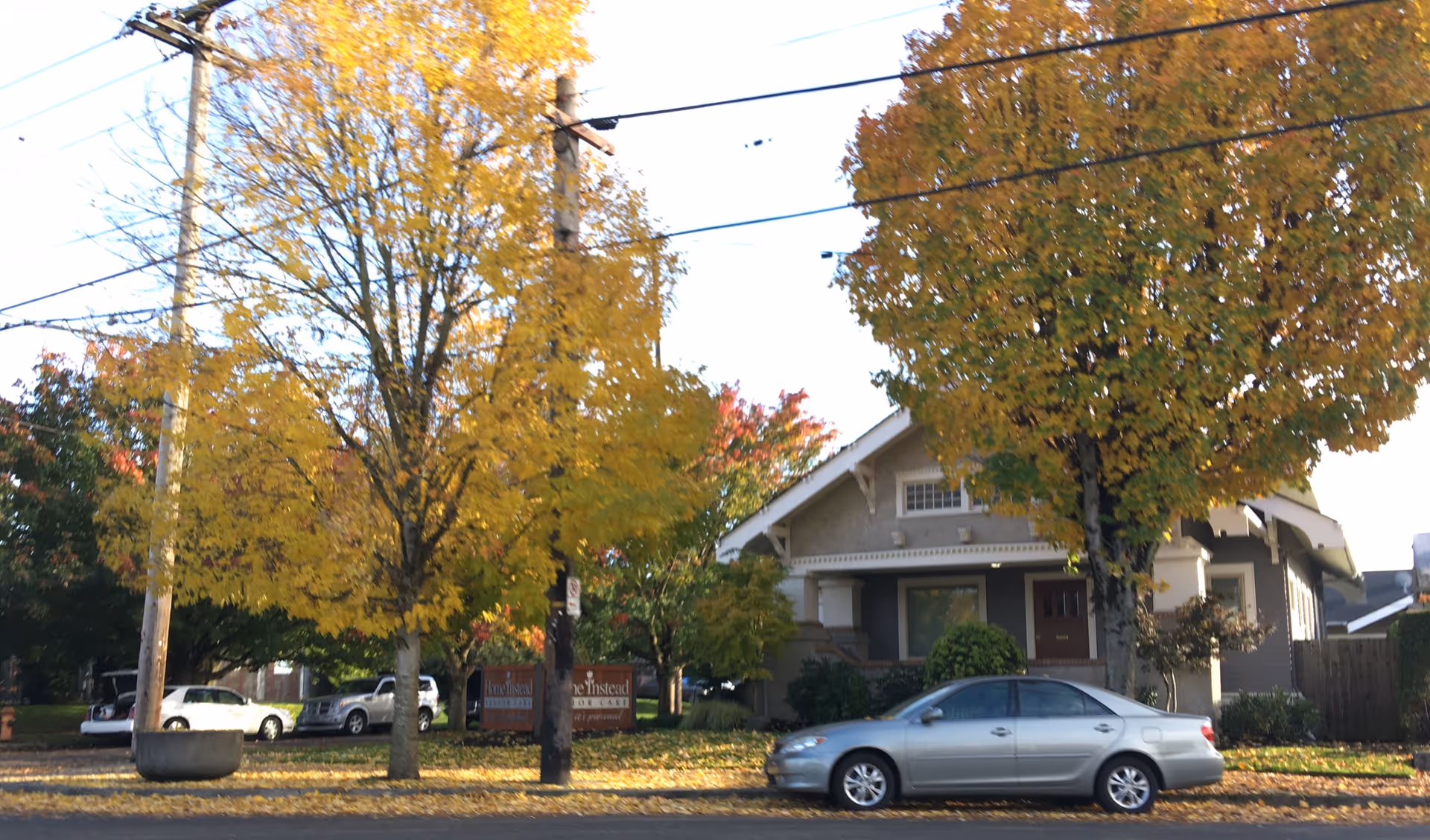 Exterior view of a residential building with a car parked along the street and autumn trees.