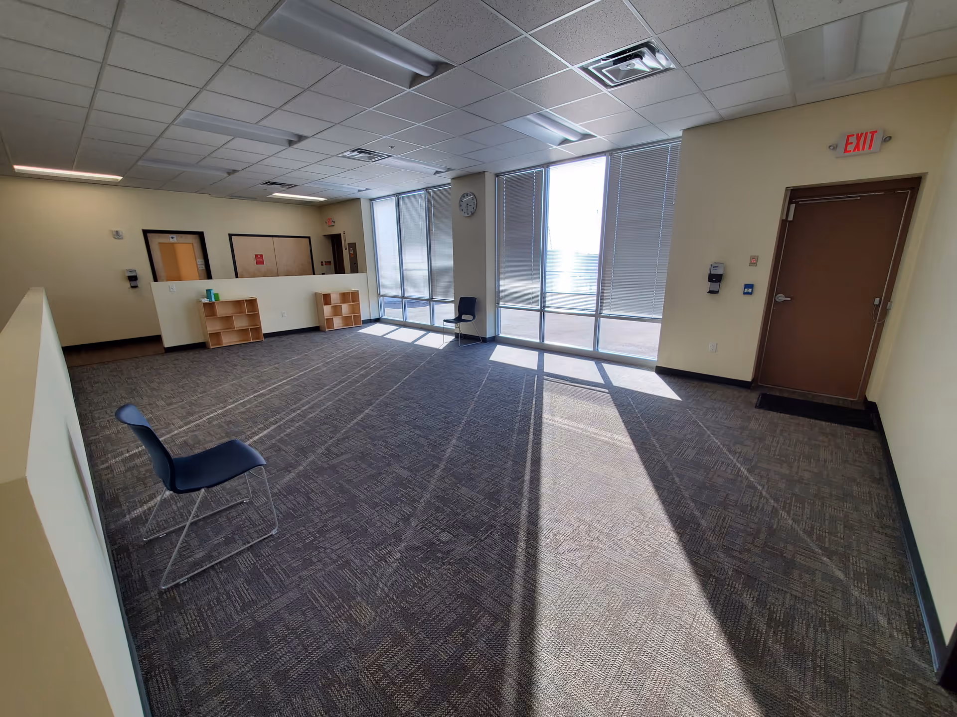A spacious empty lobby with large windows, a reception desk, and several chairs.