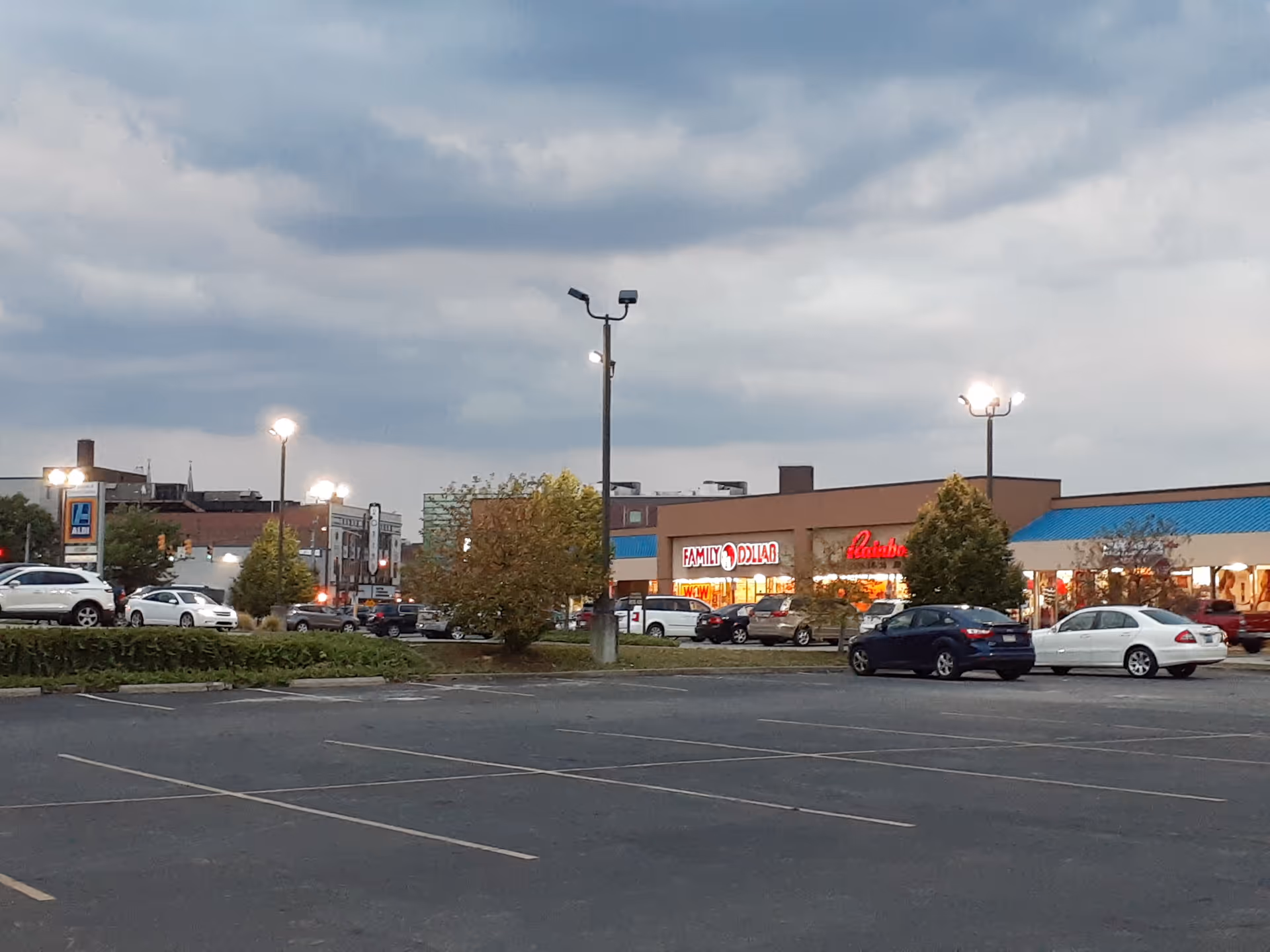 Parking lot in front of a strip mall with storefronts and lit signs