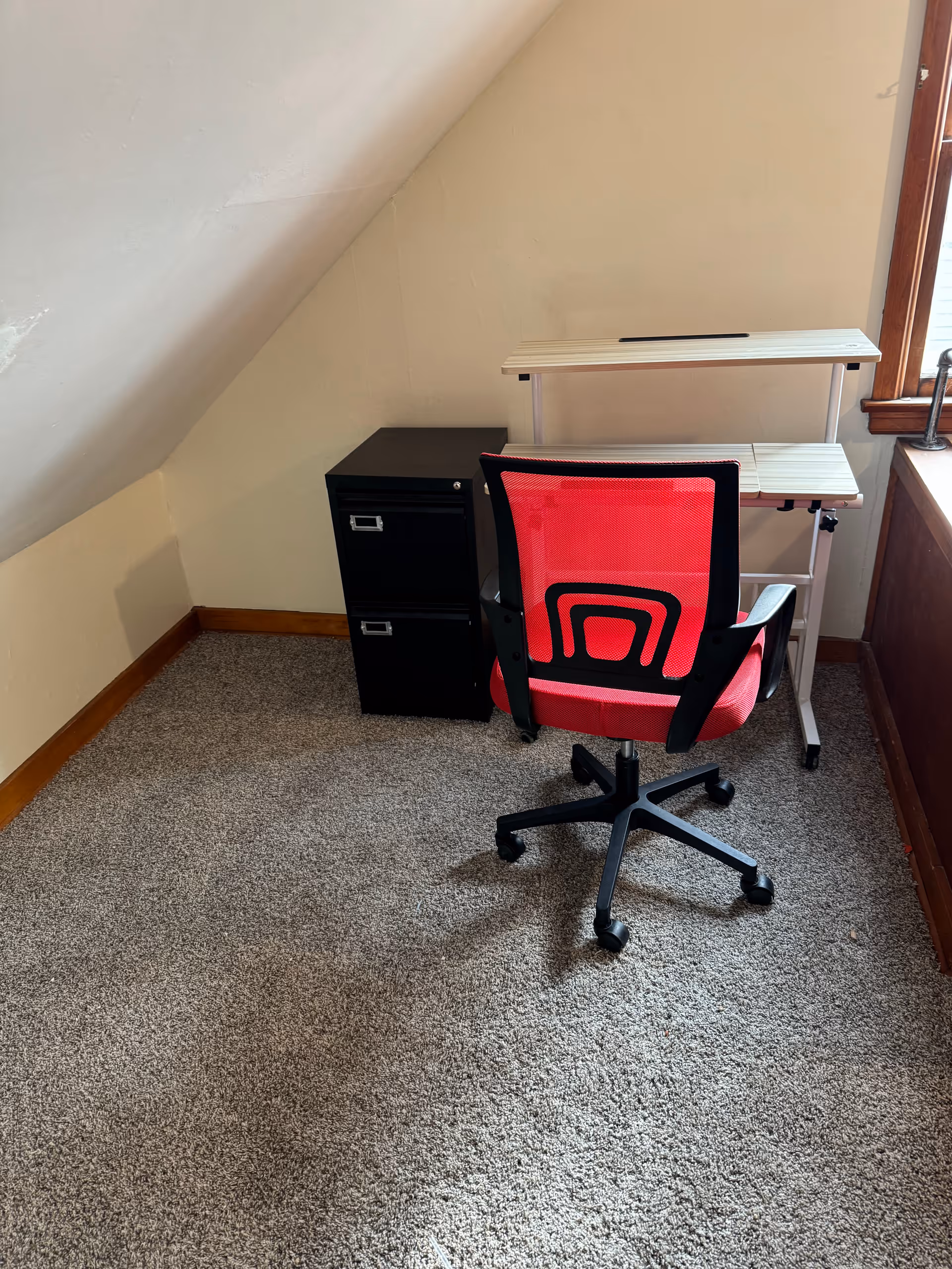 Small office nook with a red ergonomic chair, white desk, and black filing cabinet.