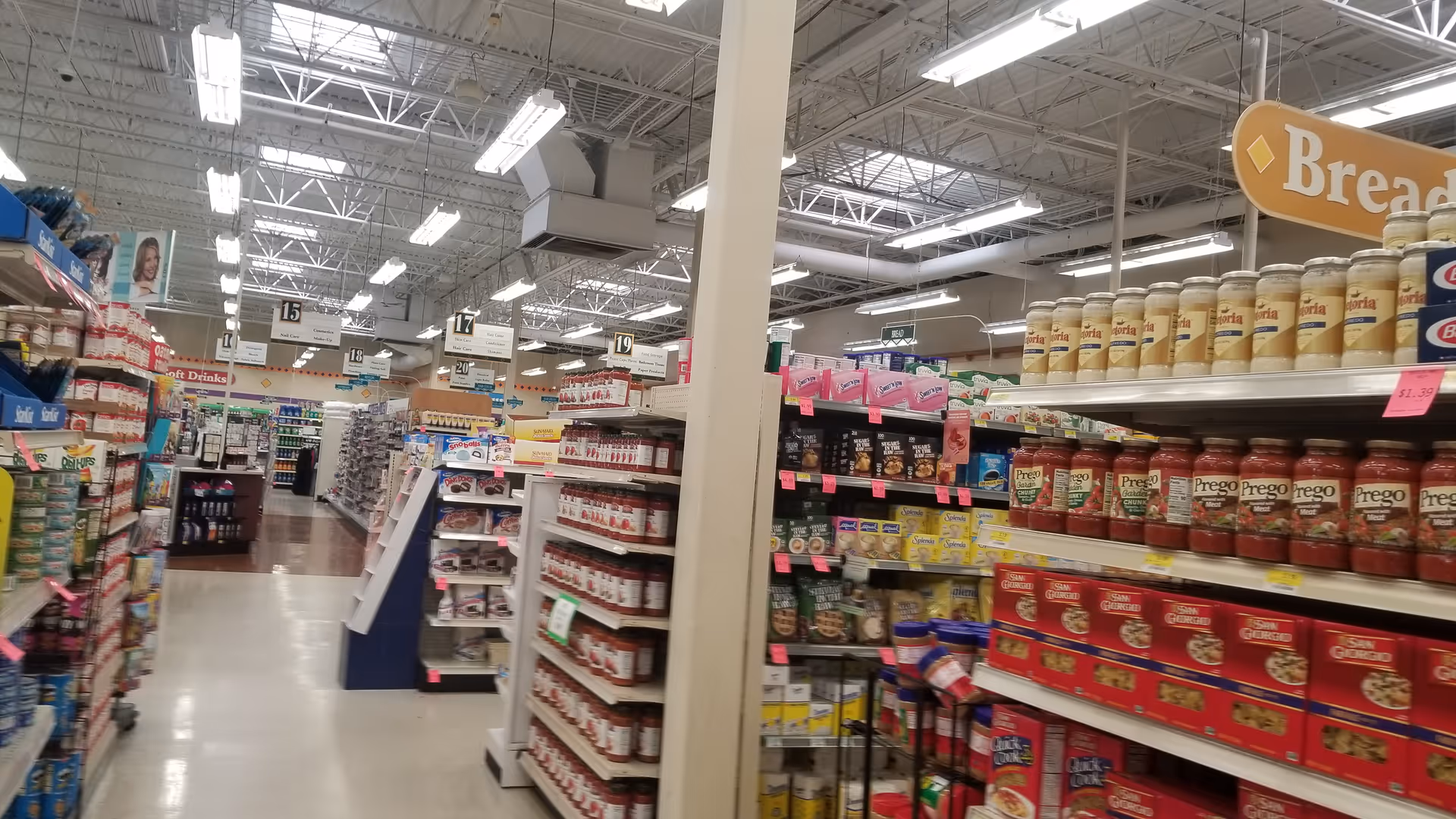 Aisles of grocery shelves inside a Discount Drug Mart store with bread section.