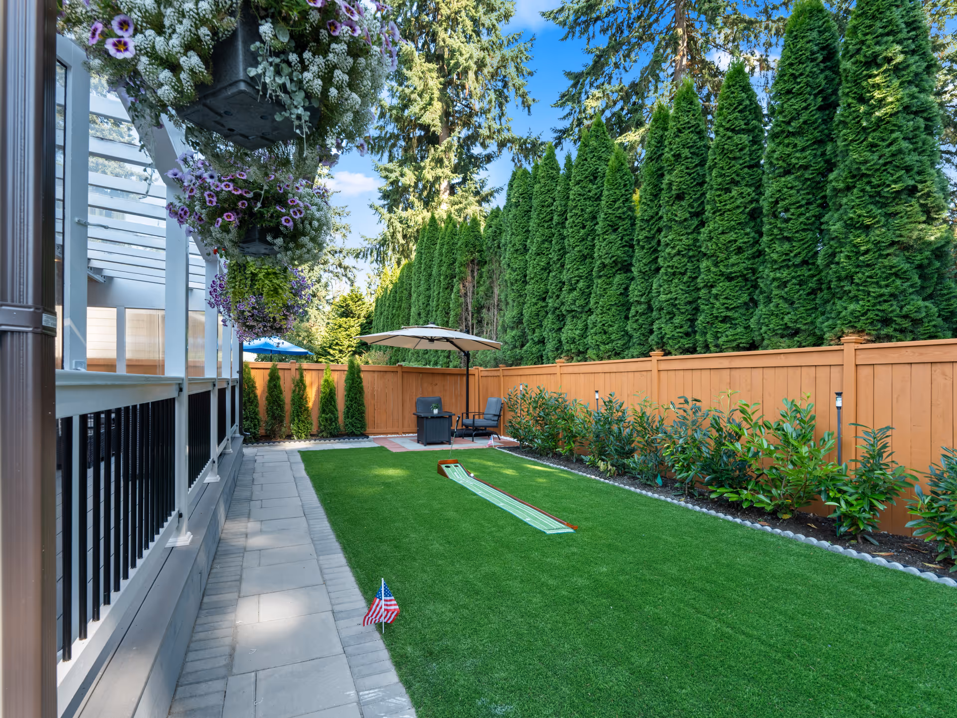 Outdoor courtyard of a senior living facility with lawn, patio seating, and hanging planters.