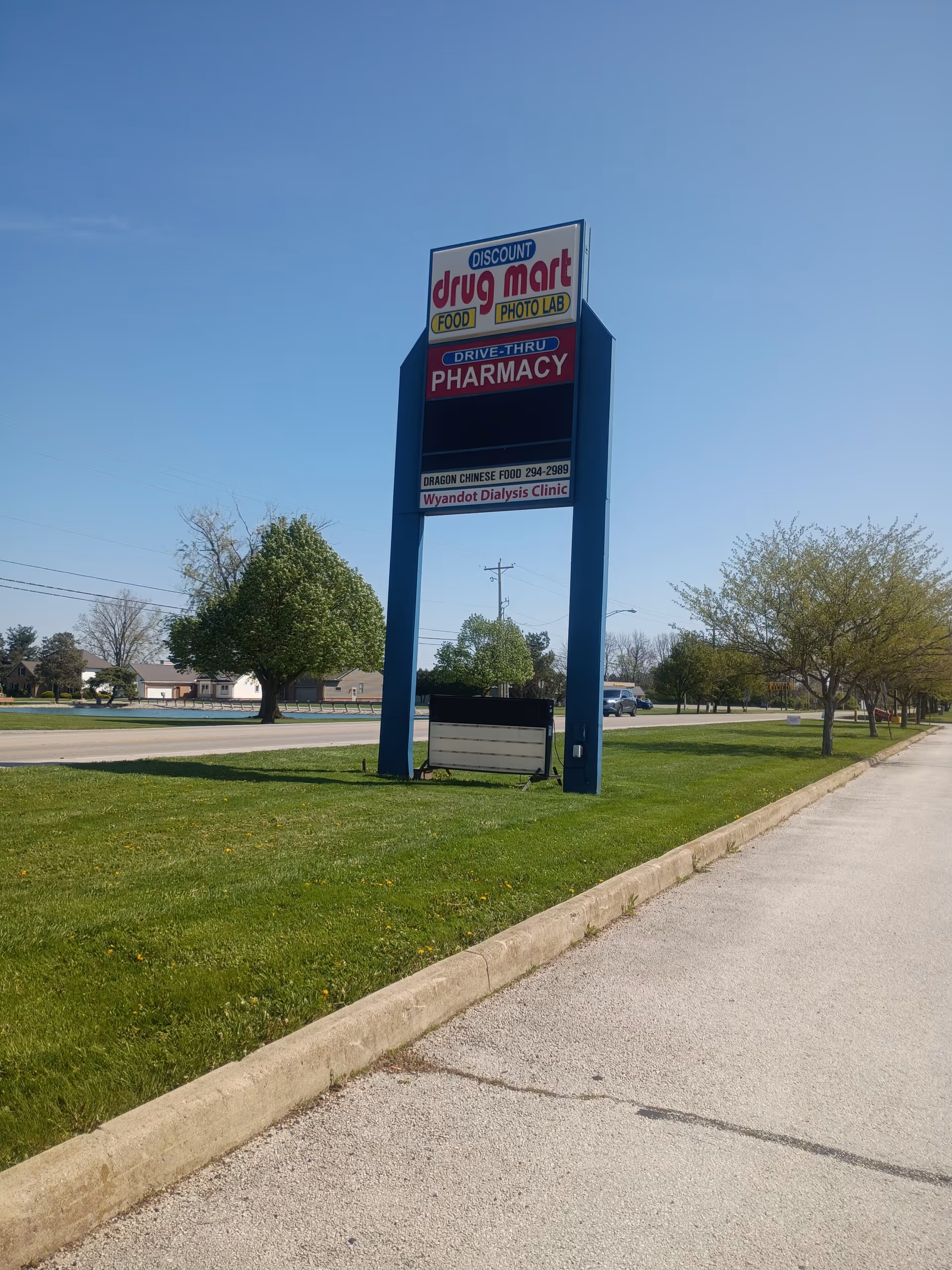 Tall blue-framed Discount Drug Mart sign beside a grassy lot and sidewalk.