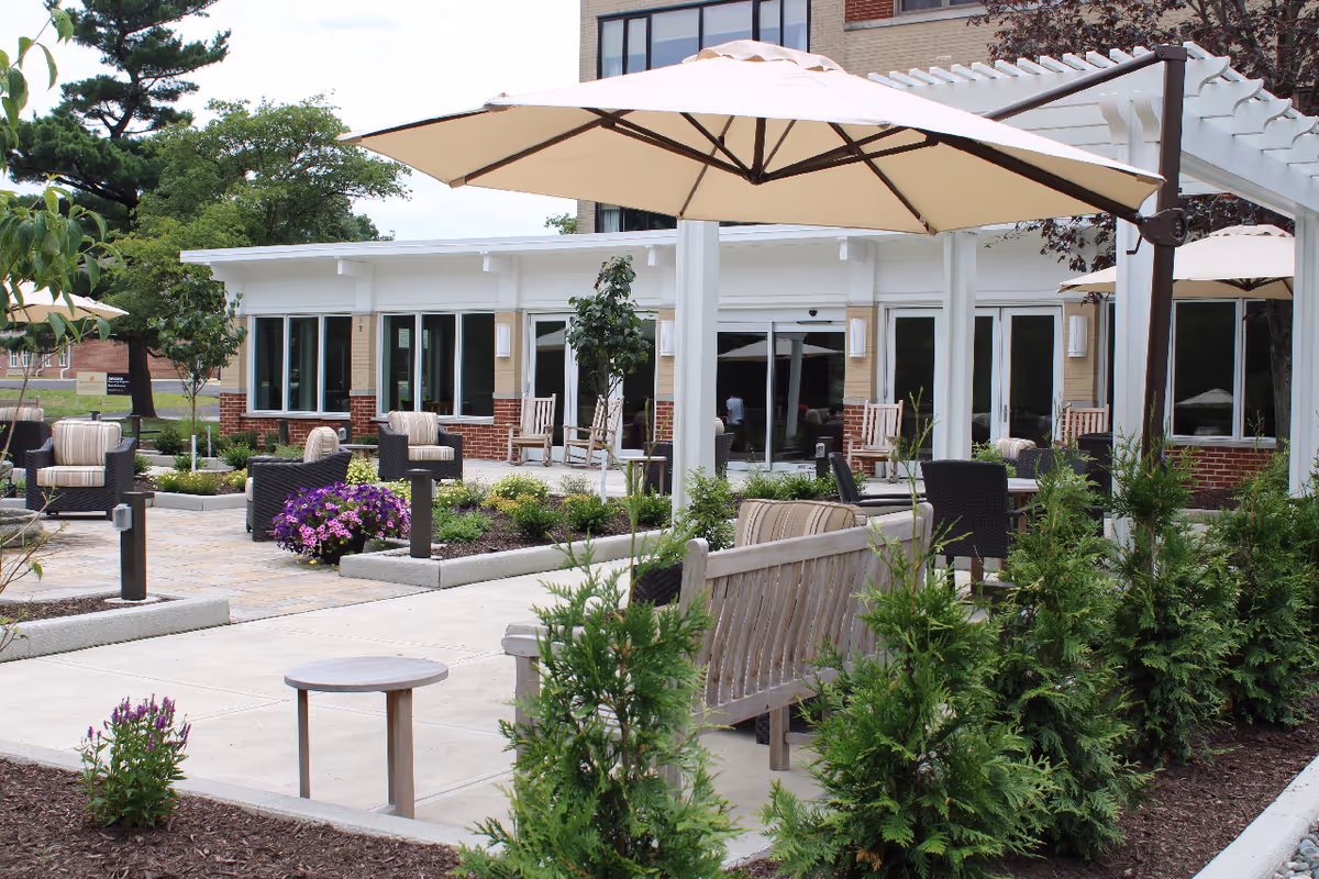 Outdoor patio of a senior facility with umbrellas, chairs, and landscaped planters.