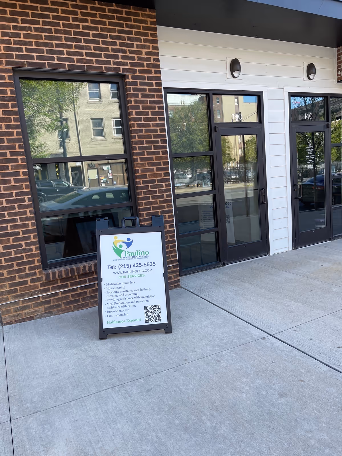 Exterior view of a brick building entrance with glass doors and a signboard.