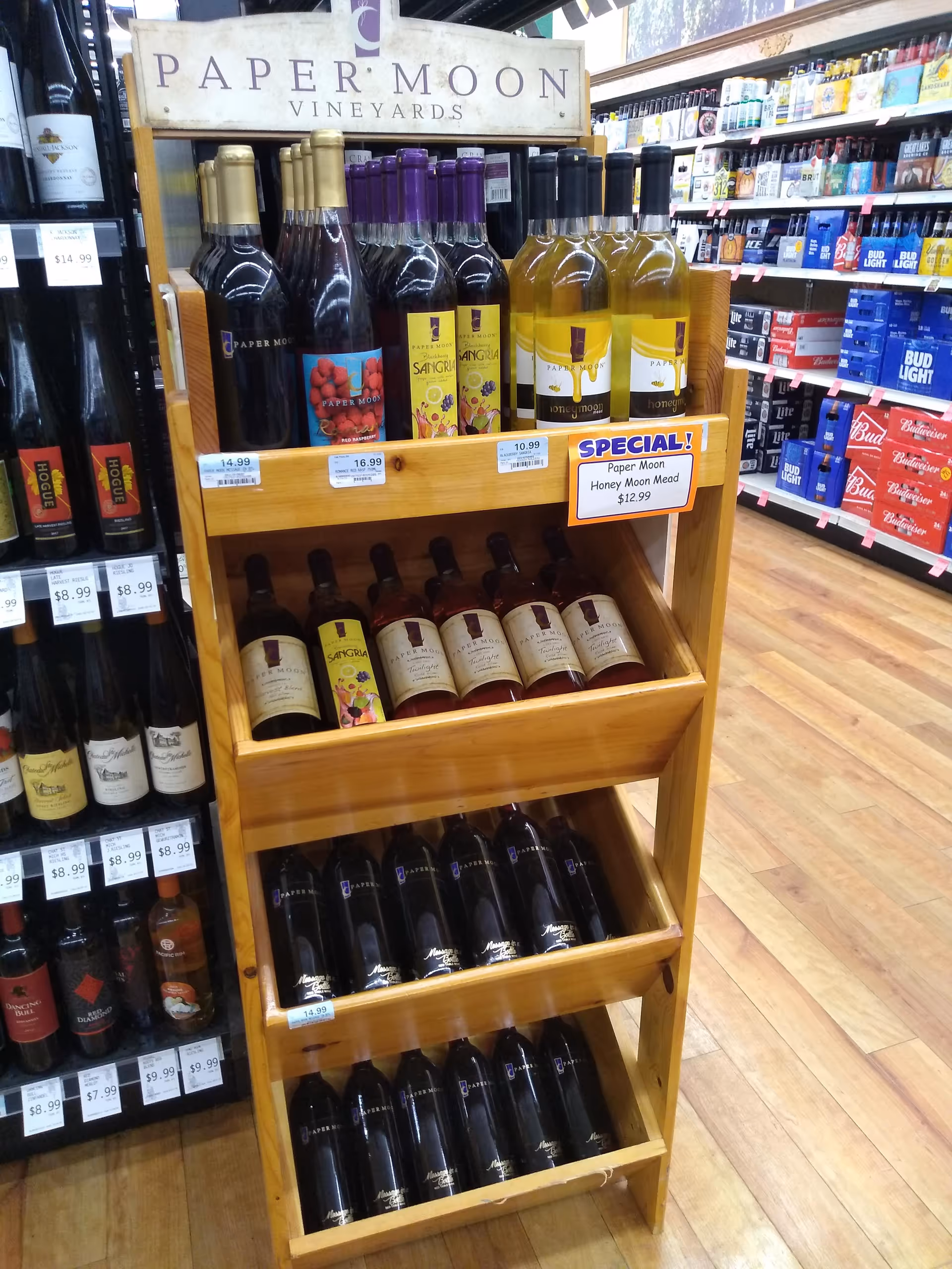Wooden wine display shelf filled with Paper Moon Vineyards bottles in a store aisle.