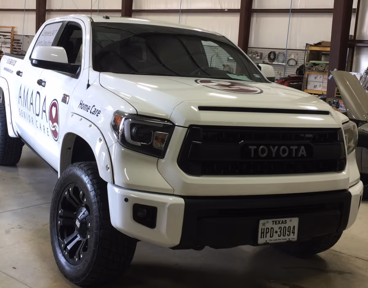 White Toyota truck with Amada Senior Care branding inside a workshop.