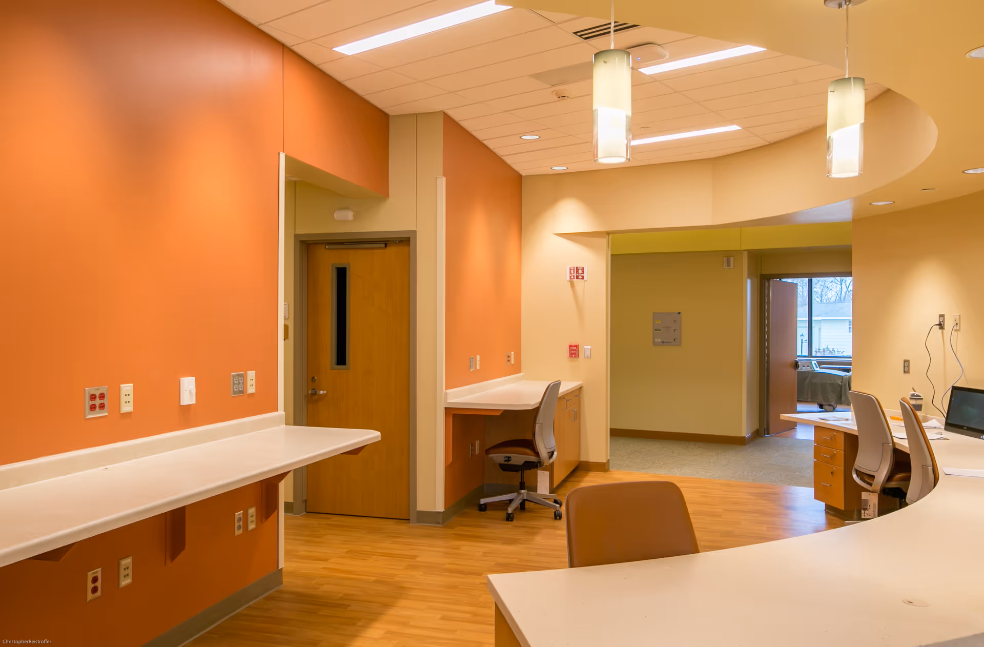 Curved white counters, orange walls, and desks create a modern interior reception area.