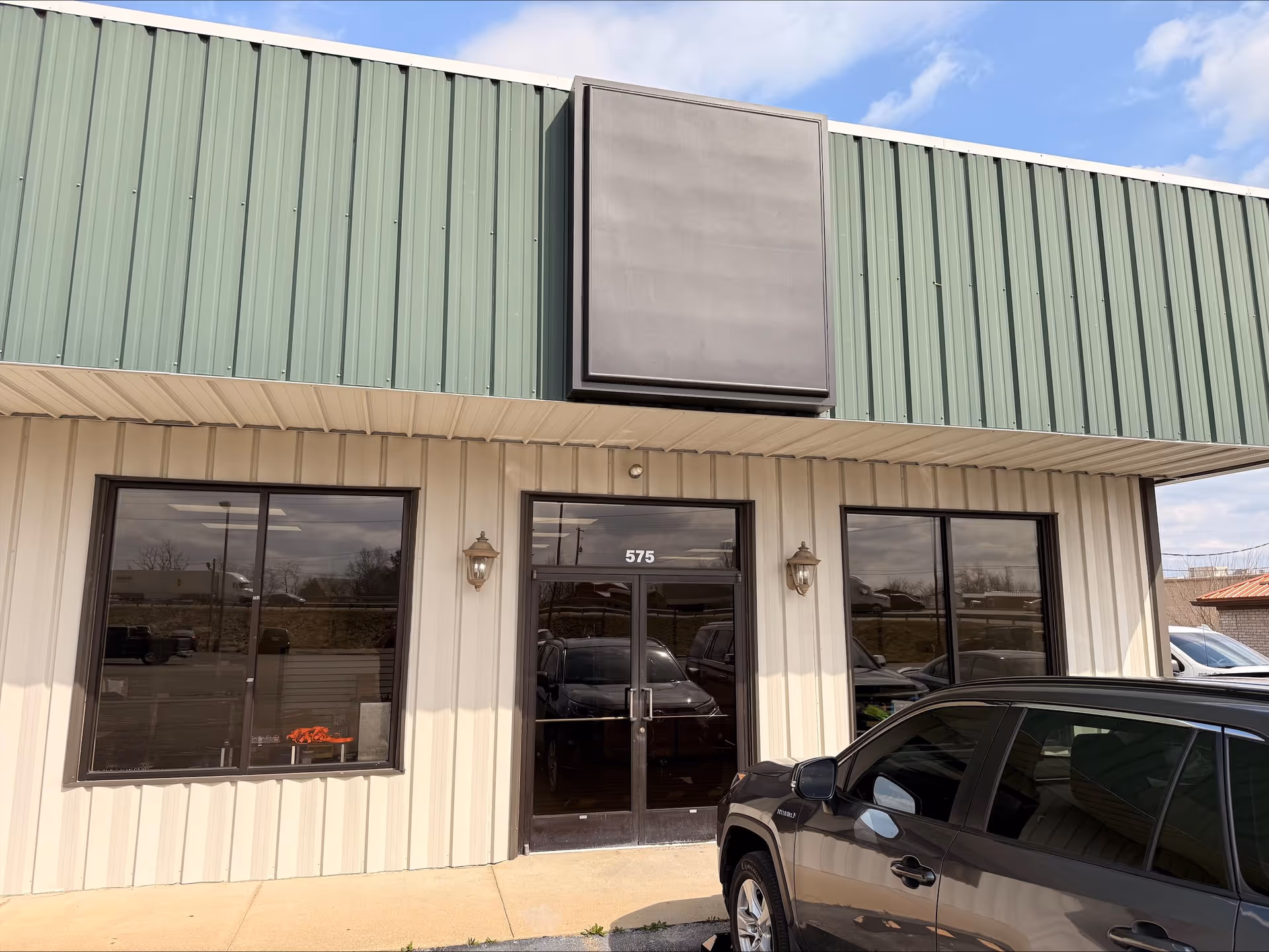 Building front of a facility with glass doors and a car parked outside.