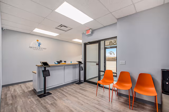 Reception area with a counter, orange chairs, and a logo on a light blue wall.