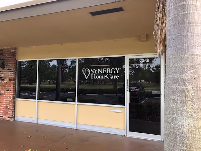 Exterior storefront of Synergy HomeCare with glass doors and logo.