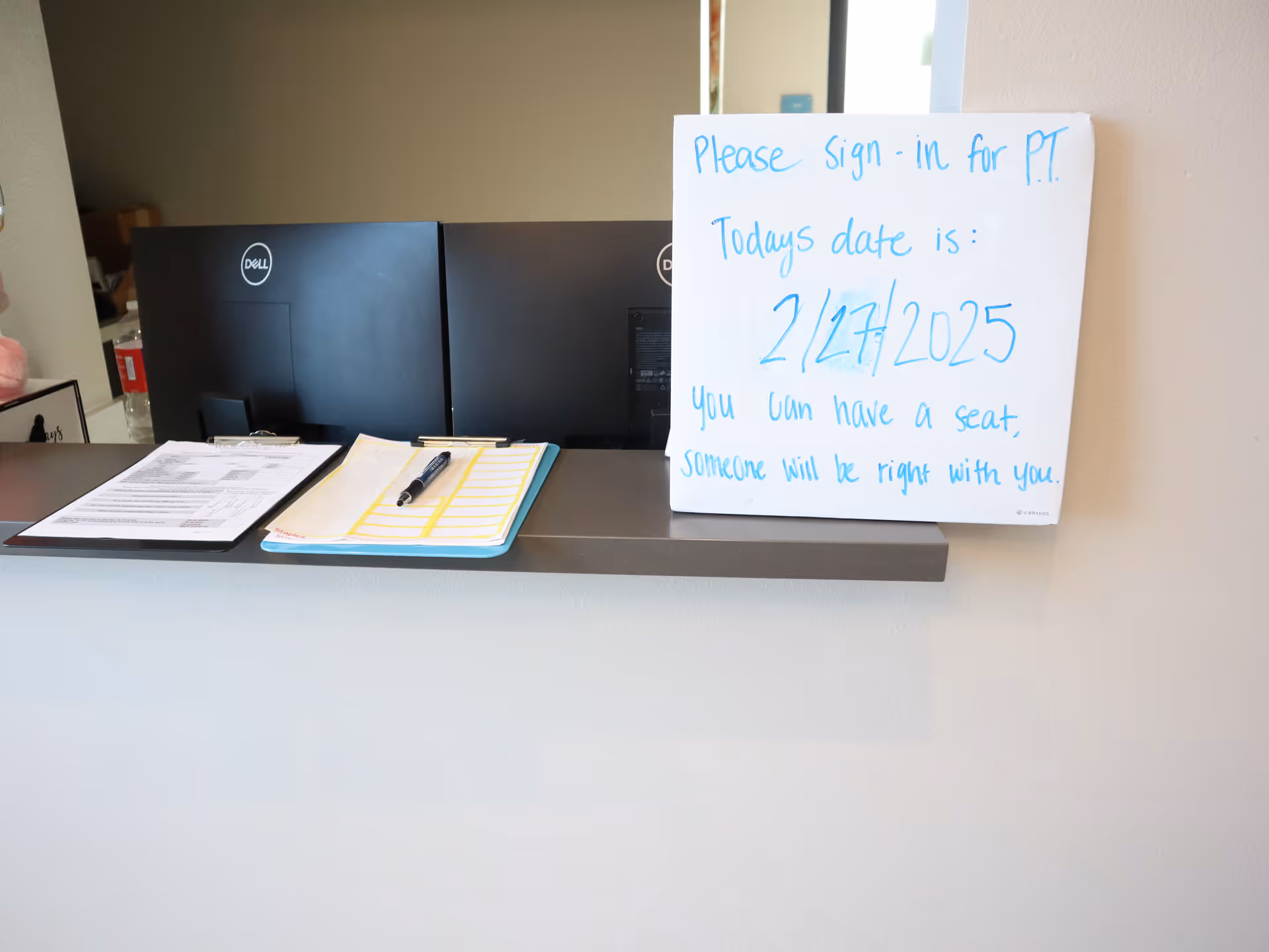 Reception desk with two Dell monitors and a handwritten sign at the counter.