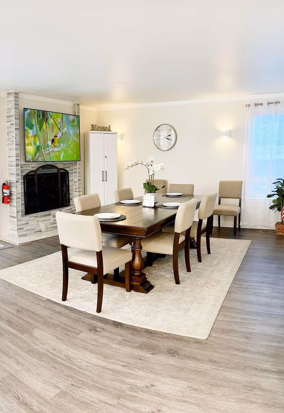 A bright dining room with a dark wood table, beige chairs, plates, and wall decor.