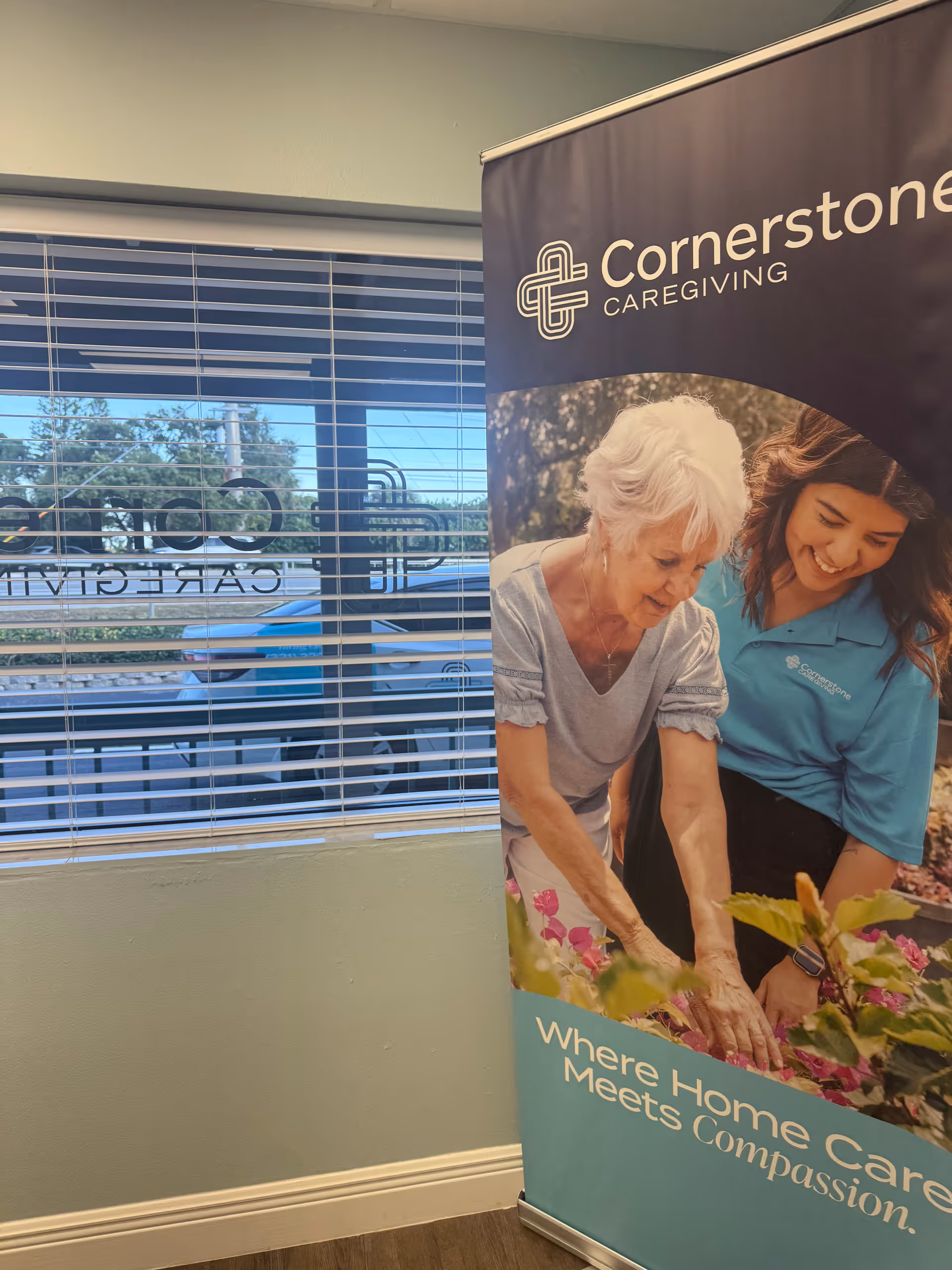 Indoor scene with Cornerstone Caregiving banner beside a window and blinds.