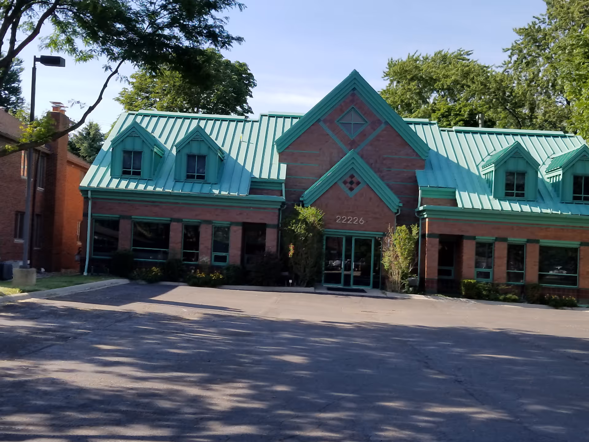 Brick building with teal roof and front entrance, surrounded by trees
