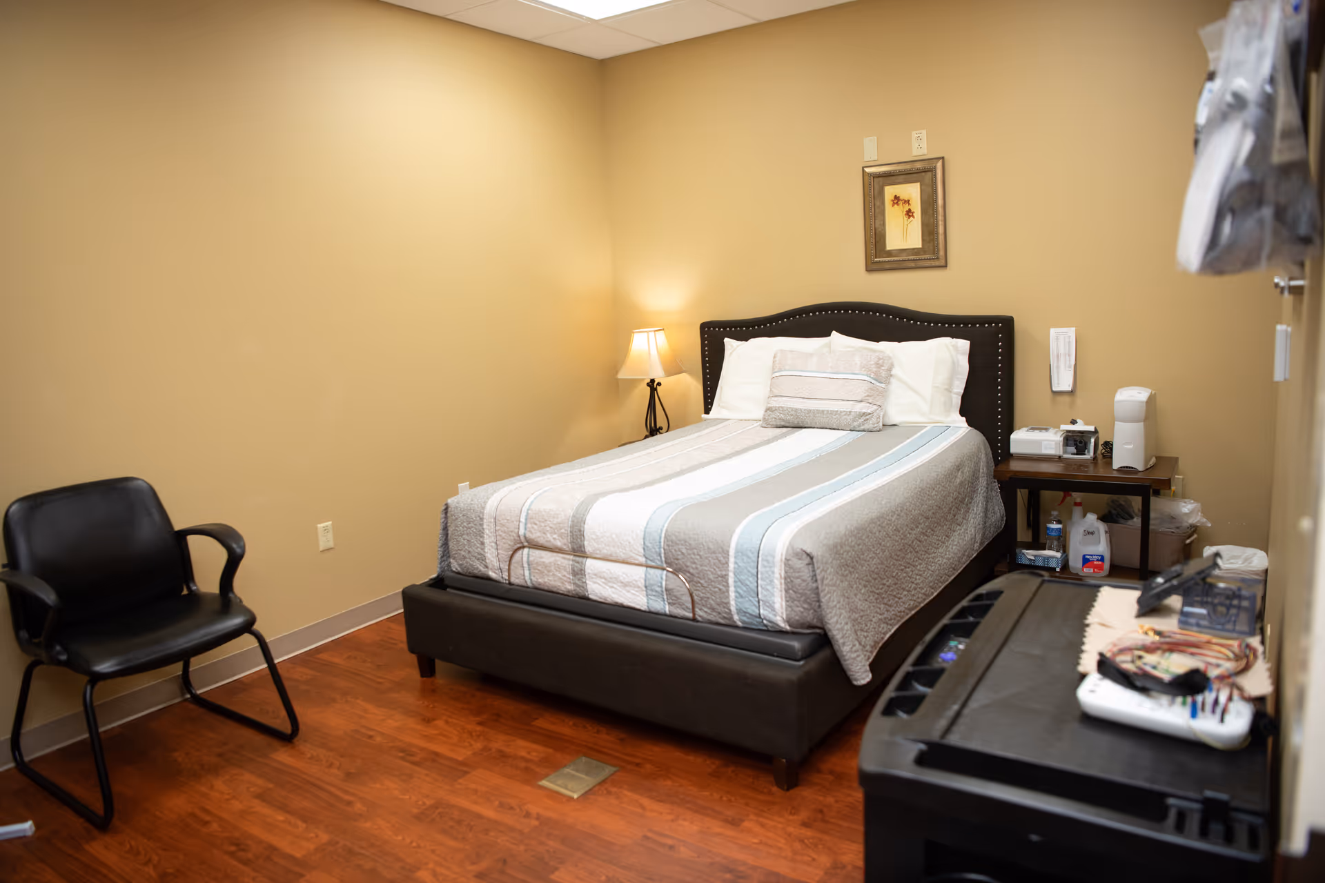 Furnished bedroom with a queen bed, nightstand, lamp, and chair.