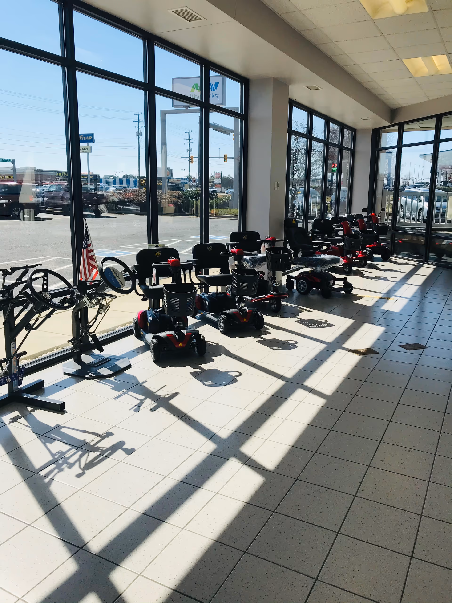 Interior showroom with multiple mobility scooters and a bicycle lined up along glass walls.