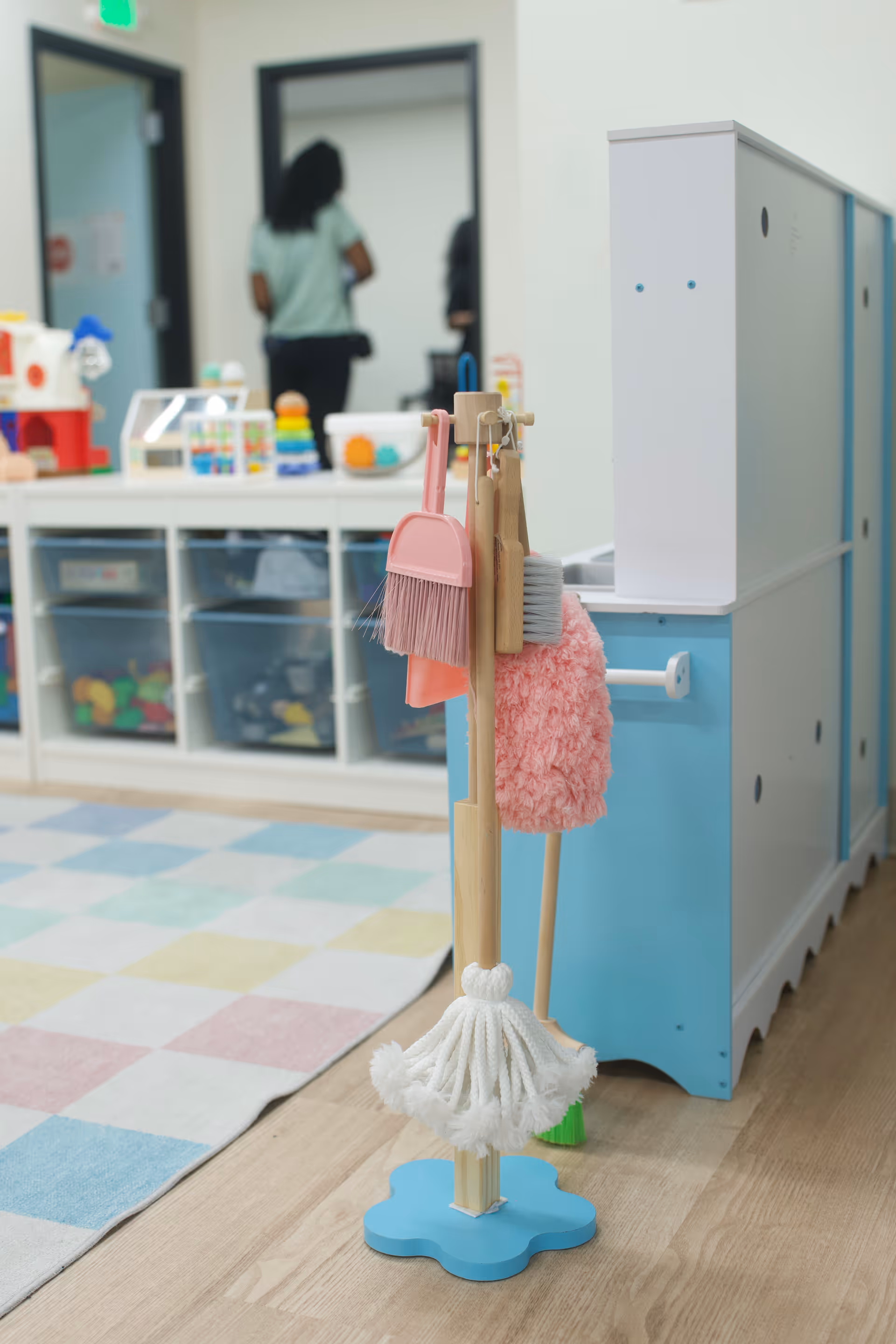 Indoor therapy room with cleaning tools, pastel rug, and toy shelves in the background.