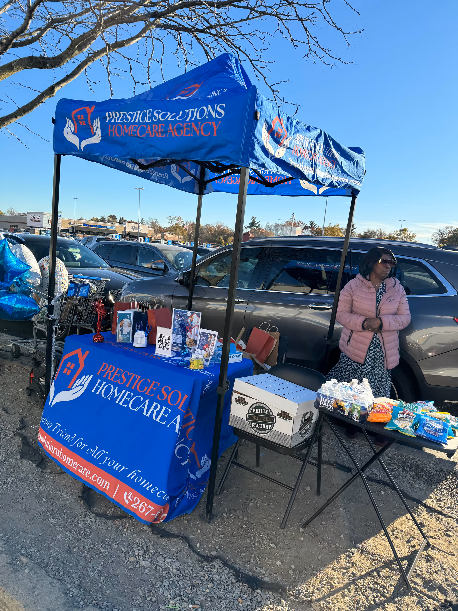 Blue canopy tent labeled Prestige Solutions HomeCare Agency covers an outdoor information booth.