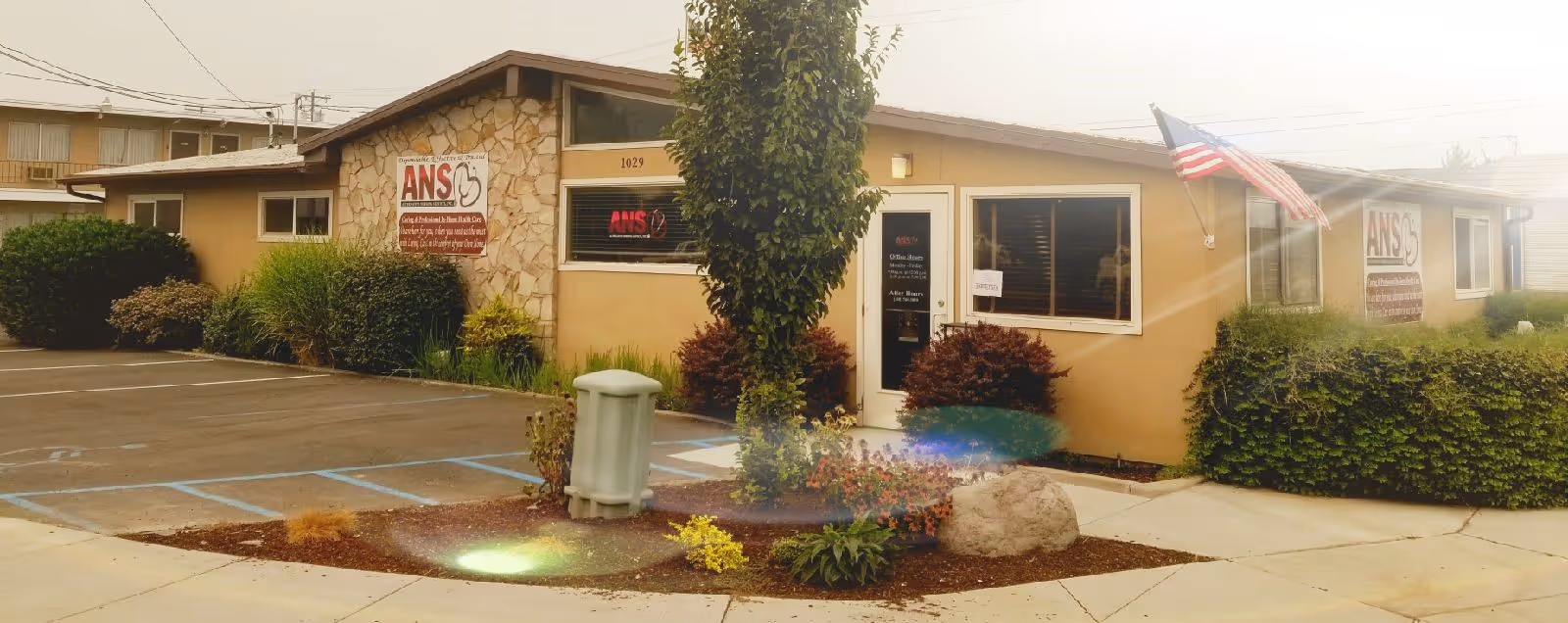 Exterior view of a beige, single-story nursing facility with ANS sign, landscaping, and parking.