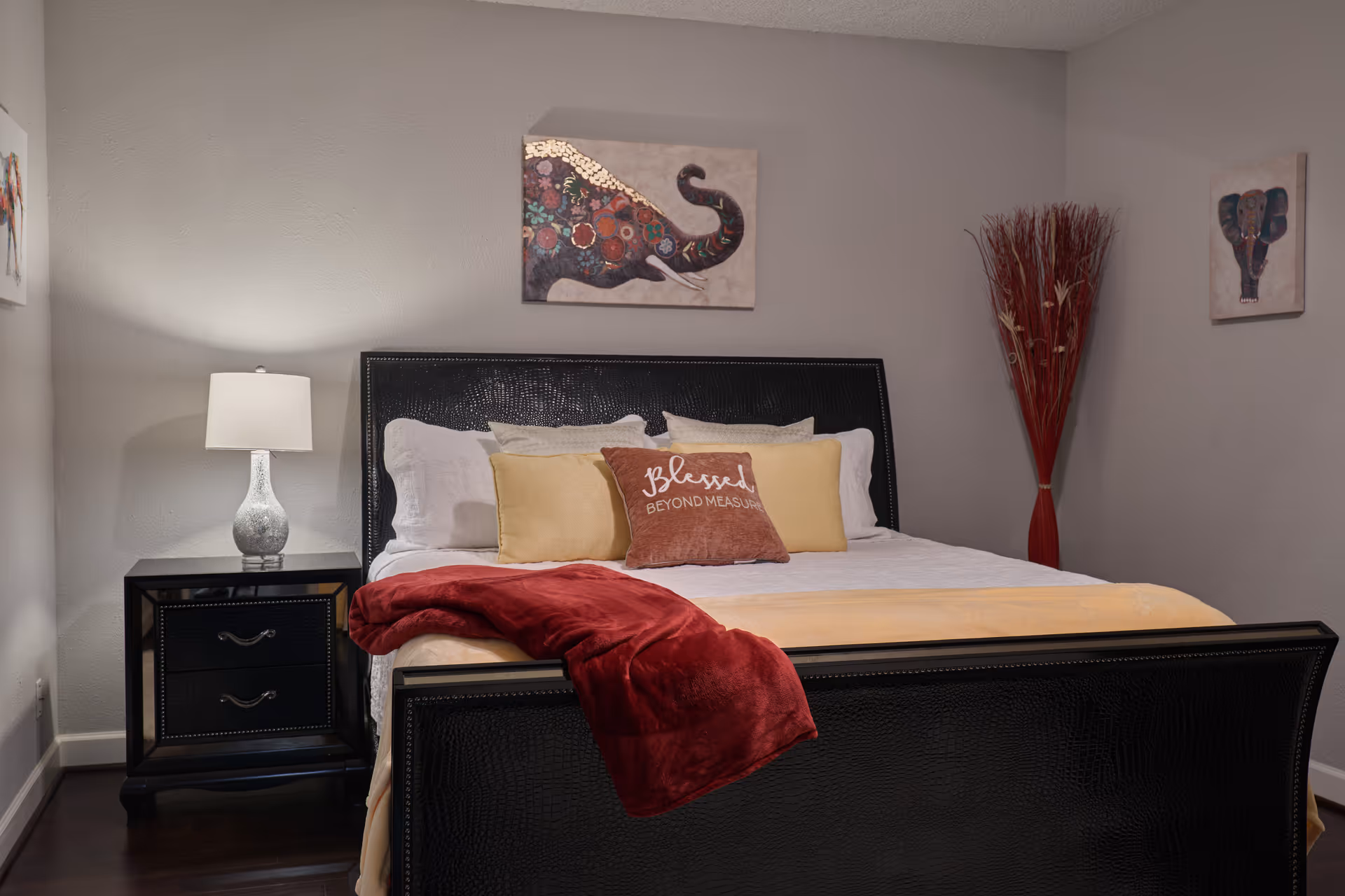 A neatly made bedroom featuring a dark headboard, pillows, and a red throw.