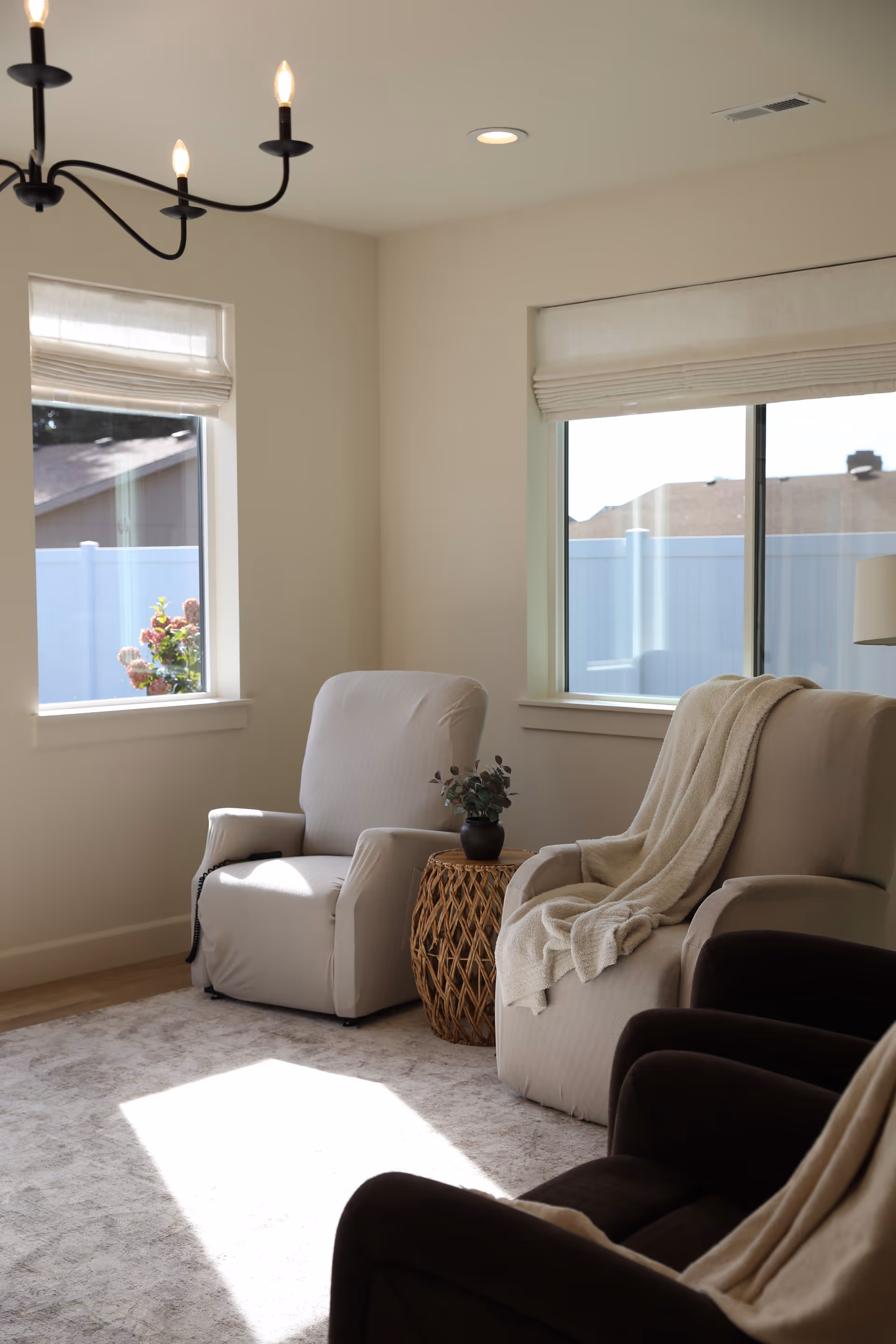 Bright living room with beige recliners, a woven side table, and large windows.