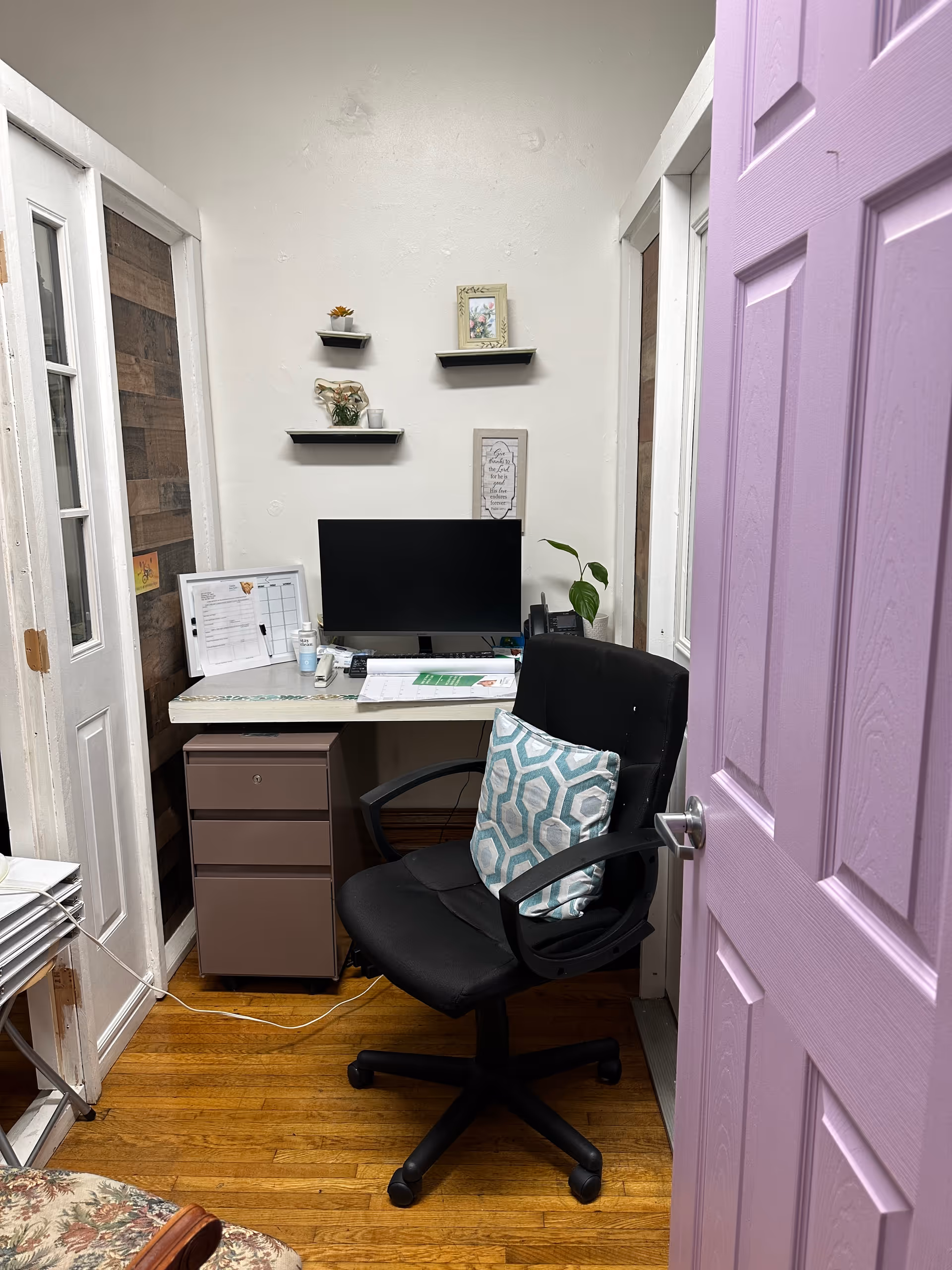 Small office nook in a facility with desk, computer, shelves, and purple door.