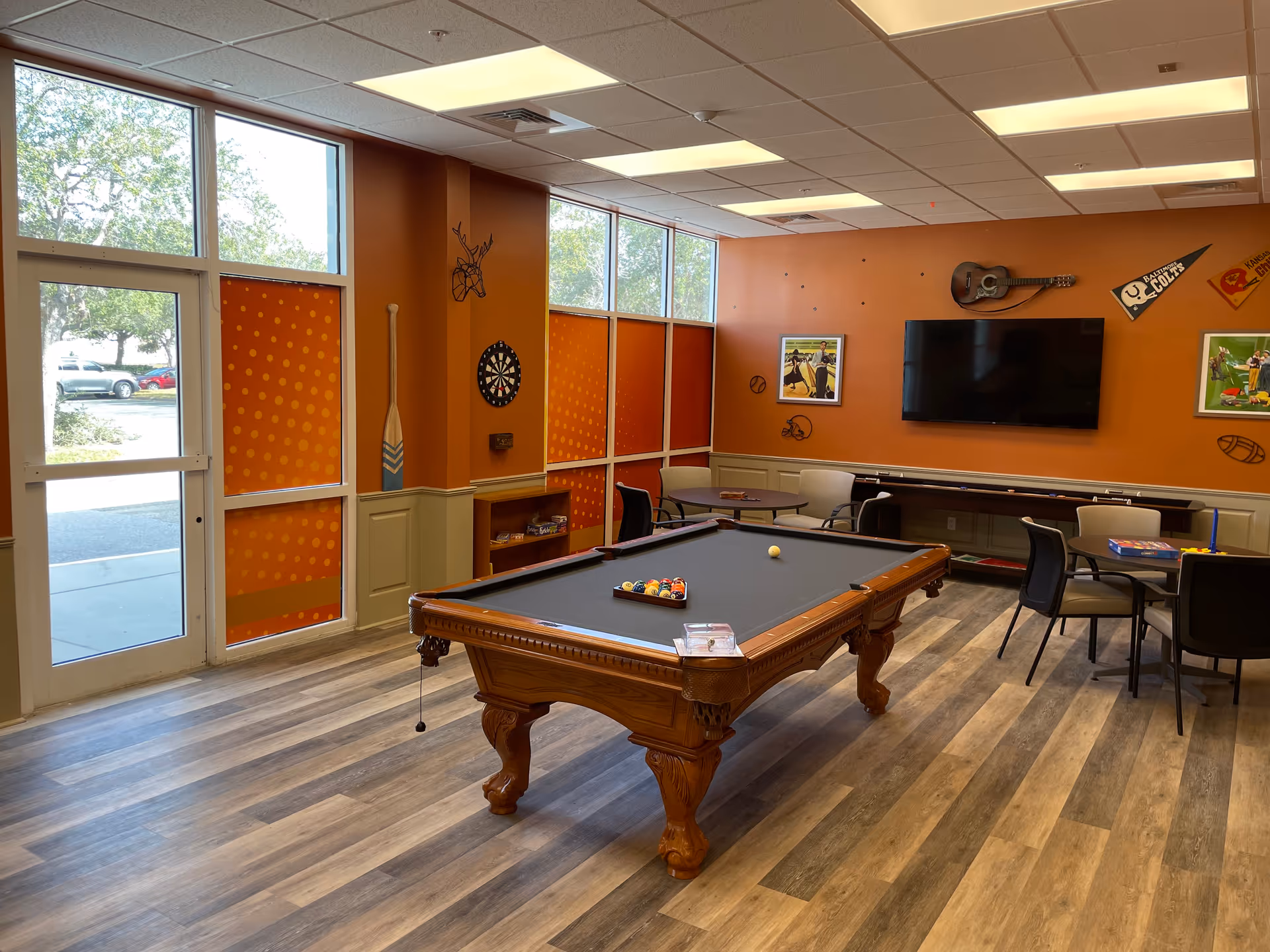 Orange-walled interior recreation room with a pool table, seating, and wall-mounted TV.
