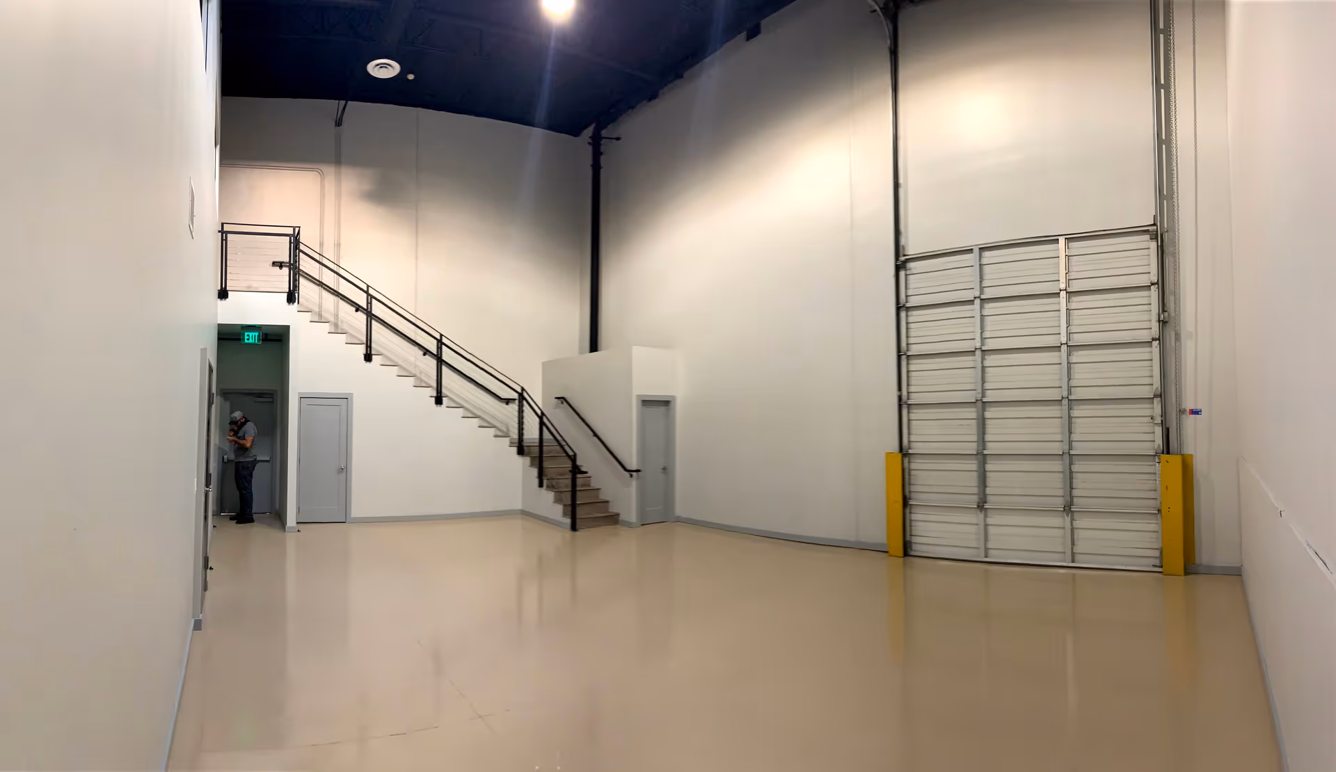 A large, empty industrial-style interior with a stairway, loading door, and minimal furnishings.
