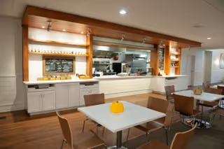 Dining area with white tables, tan chairs, and a service counter with chalkboard menu.