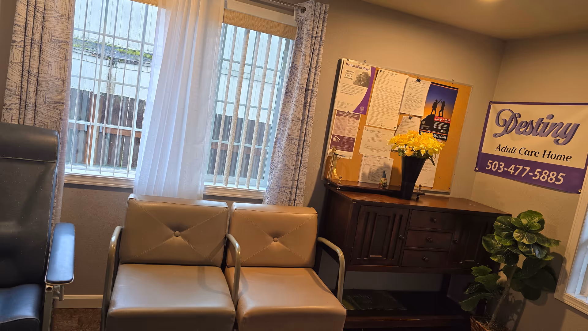 Interior waiting area with beige chairs, bulletin board, banner, and a potted plant.