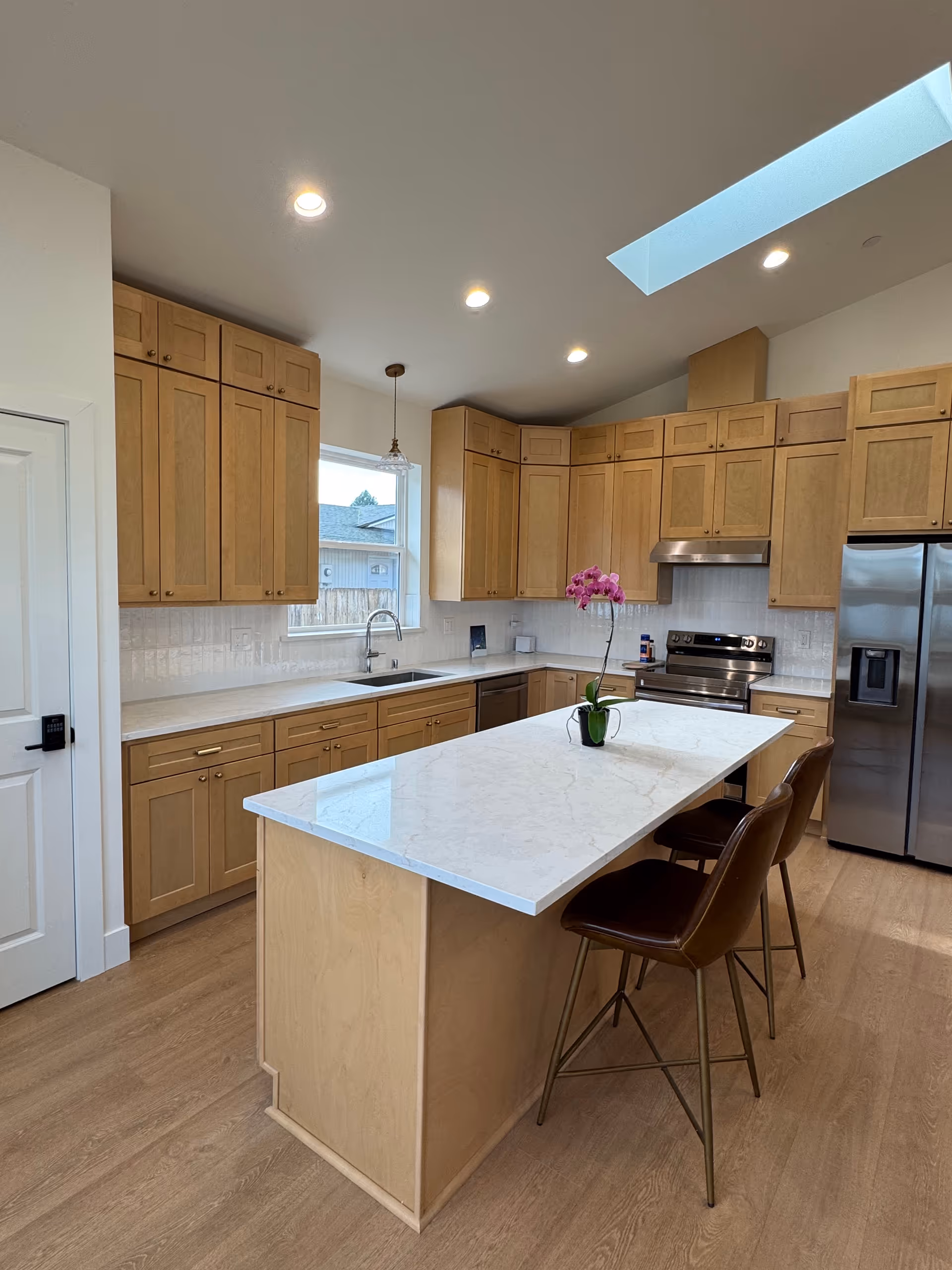 Modern kitchen at Stillwater Care Home with marble island, wood cabinets, and skylight.