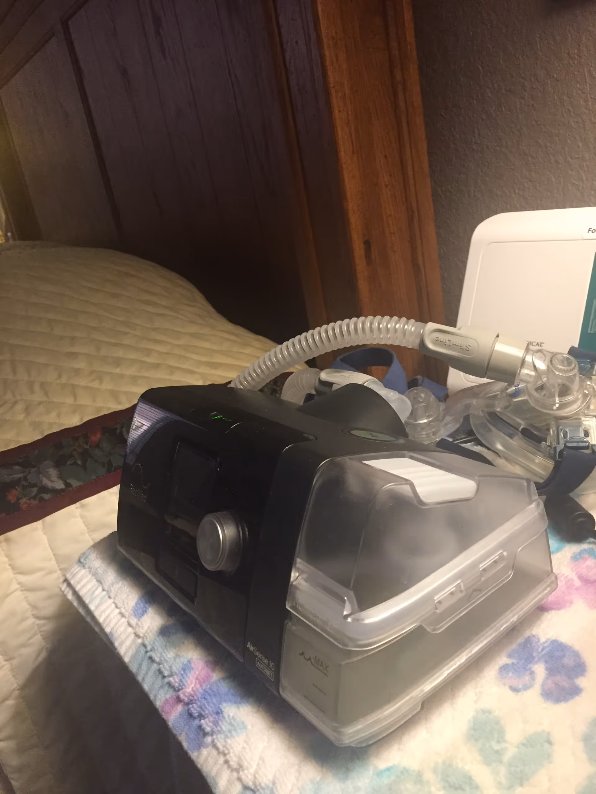 CPAP machine and tubing sit on a quilted bed in a bedroom