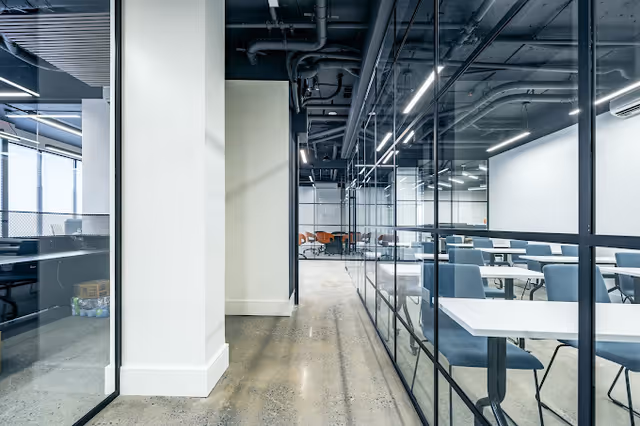 Modern interior hallway leading to a bright communal dining area with glass walls.