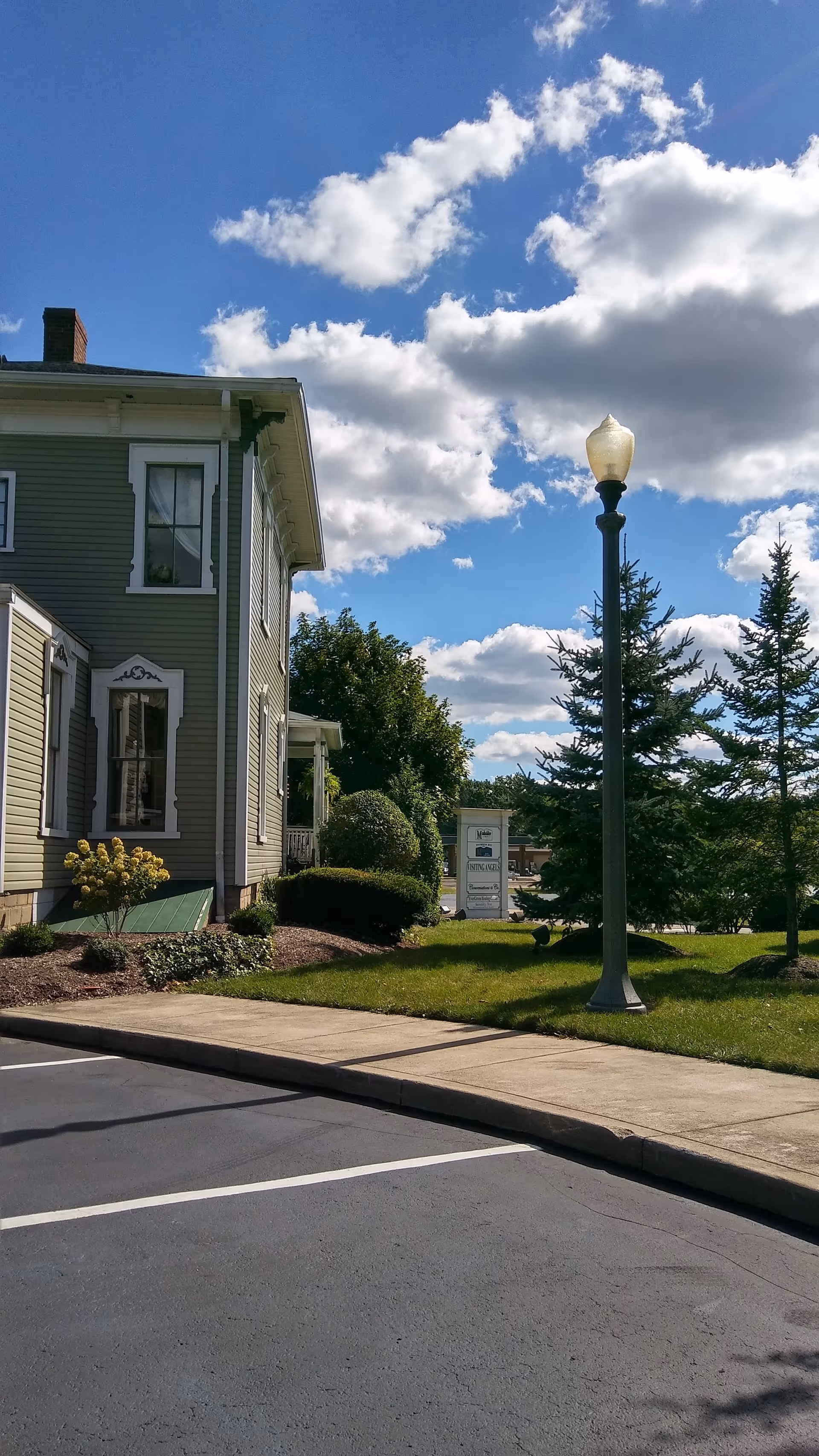 Exterior view of a green senior home with a lamp post, sidewalk, and landscaping.