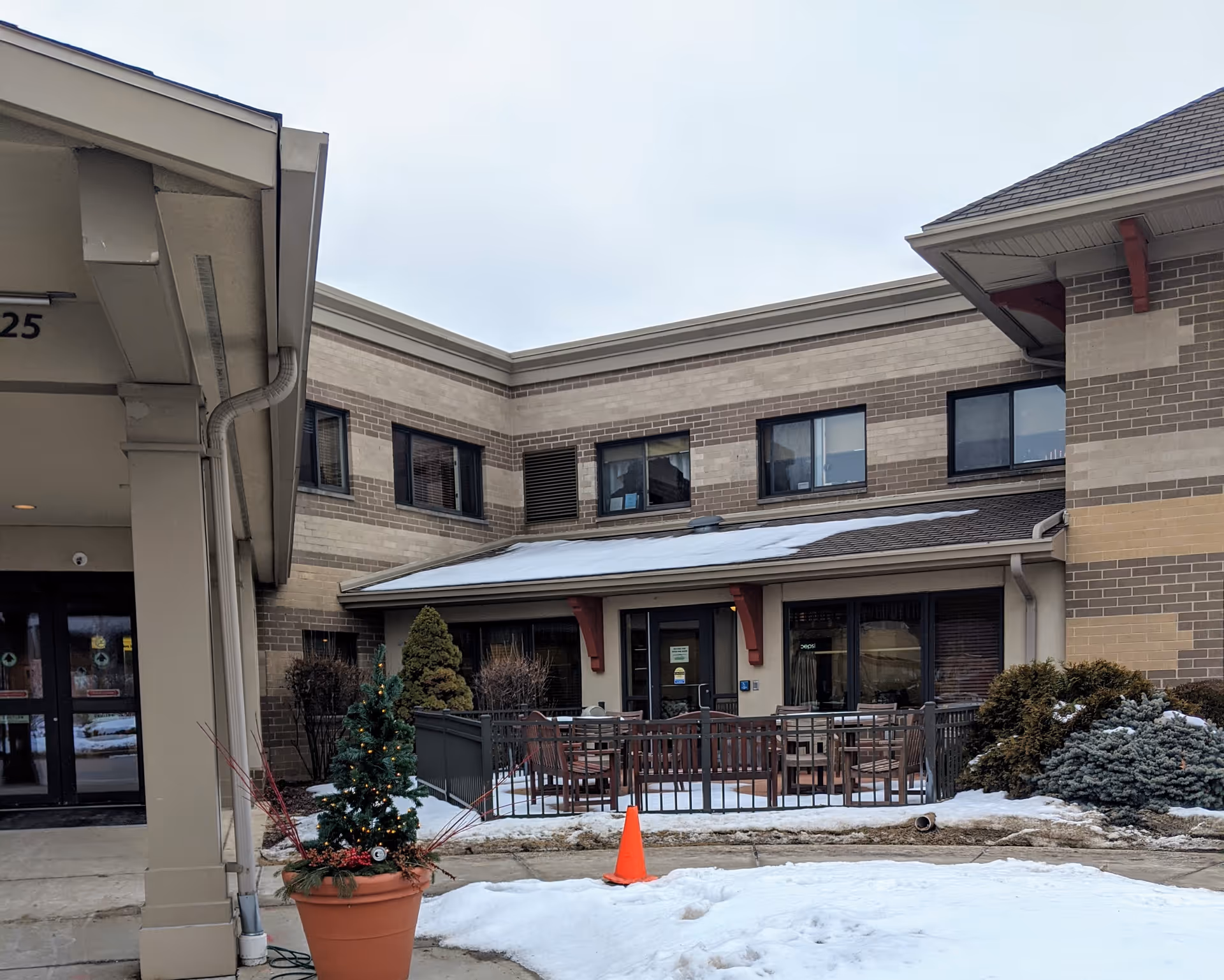 Exterior view of St Camillus Home Hospice building with snow, outdoor seating, and a potted plant.