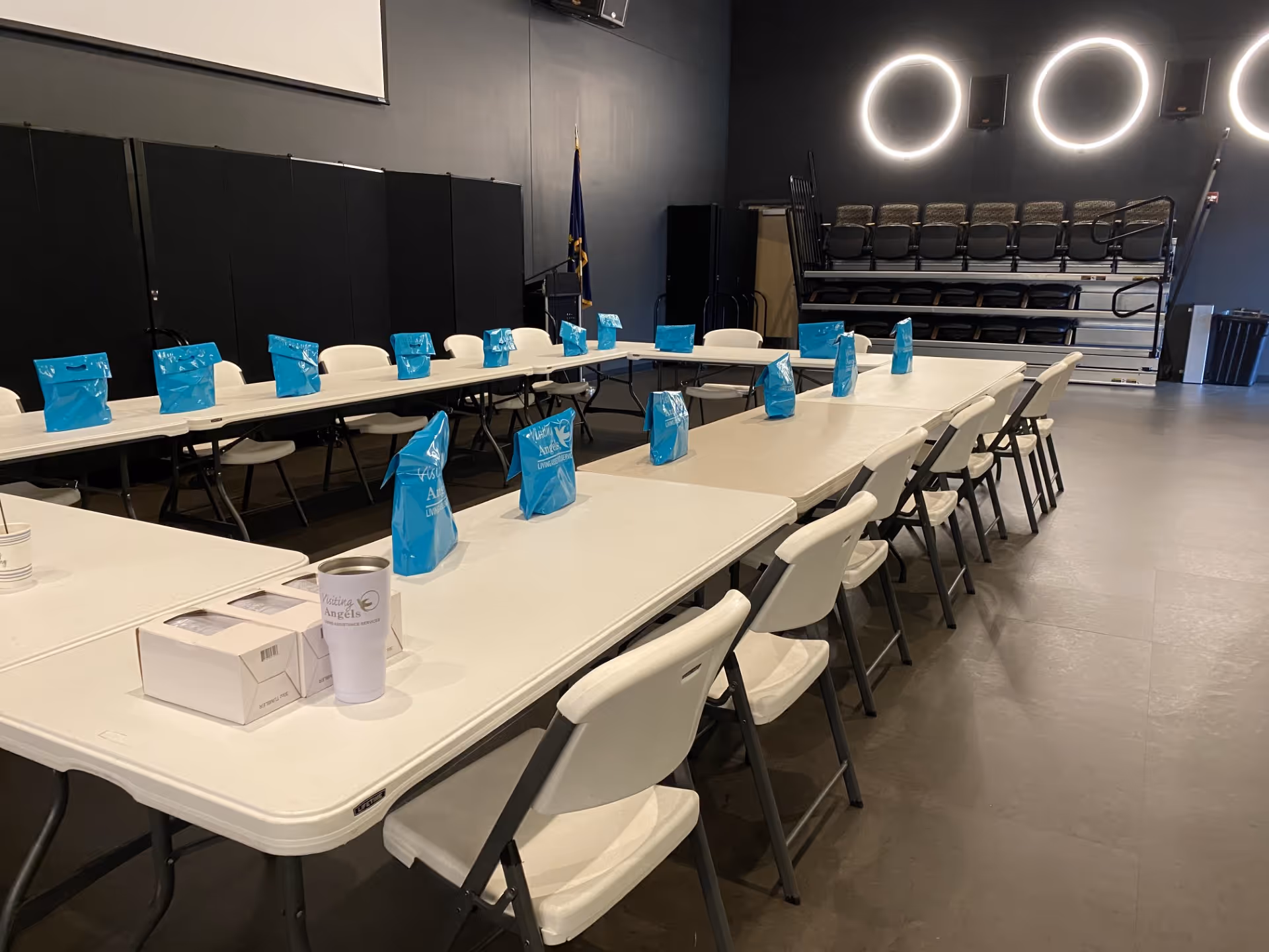 A conference room with long tables, white chairs, and blue gift bags set for an event.