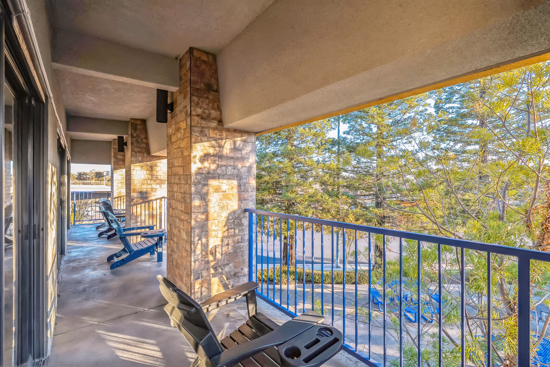 Outdoor balcony at a senior living facility with stone columns, railing, and blue chairs.