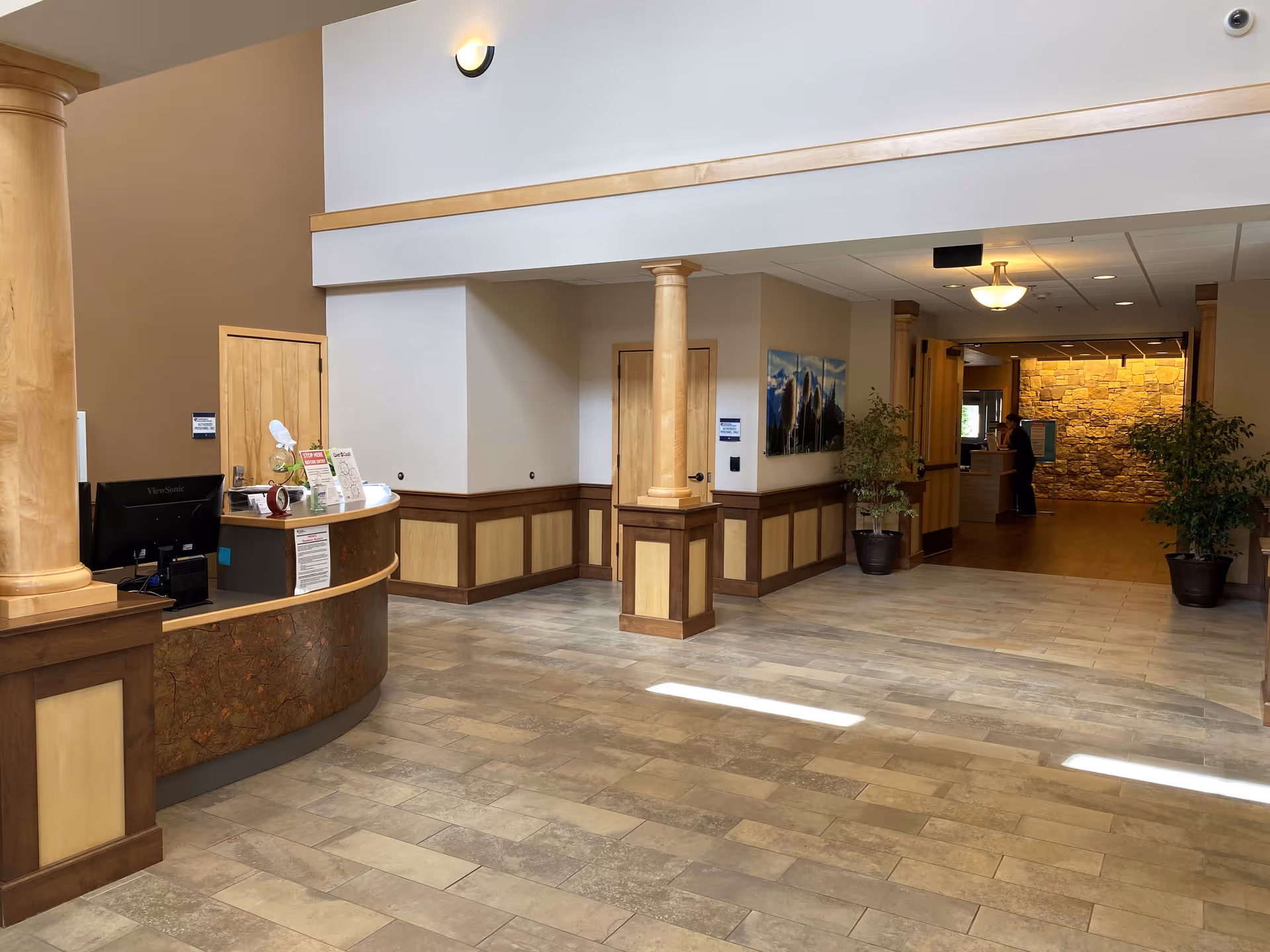 Lobby reception area with curved desk, columns, wood paneling, and potted plants.