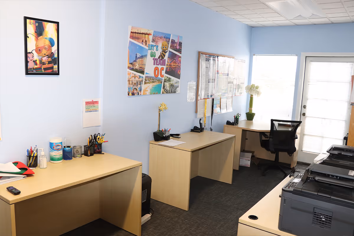 Light blue office area with desks, chairs, a large printer, and wall decor.