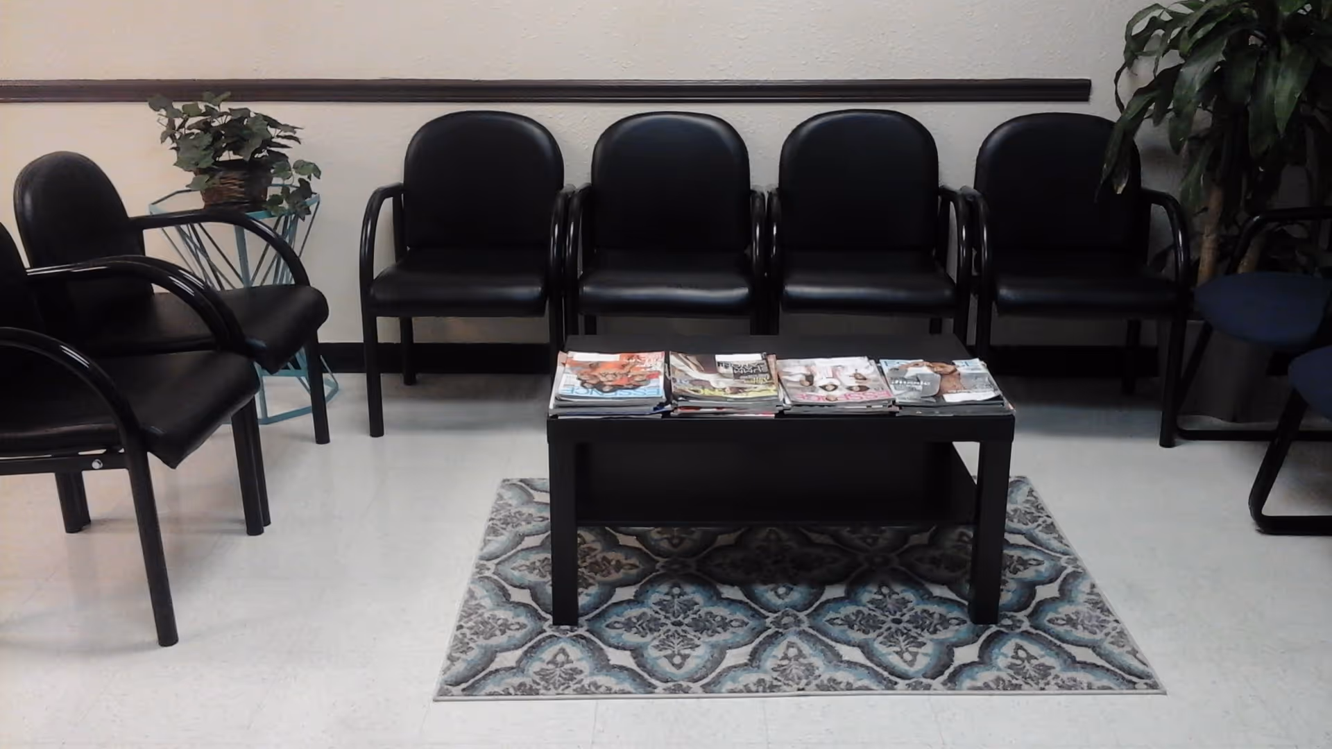 Waiting area with black chairs around a coffee table and magazines on a patterned rug