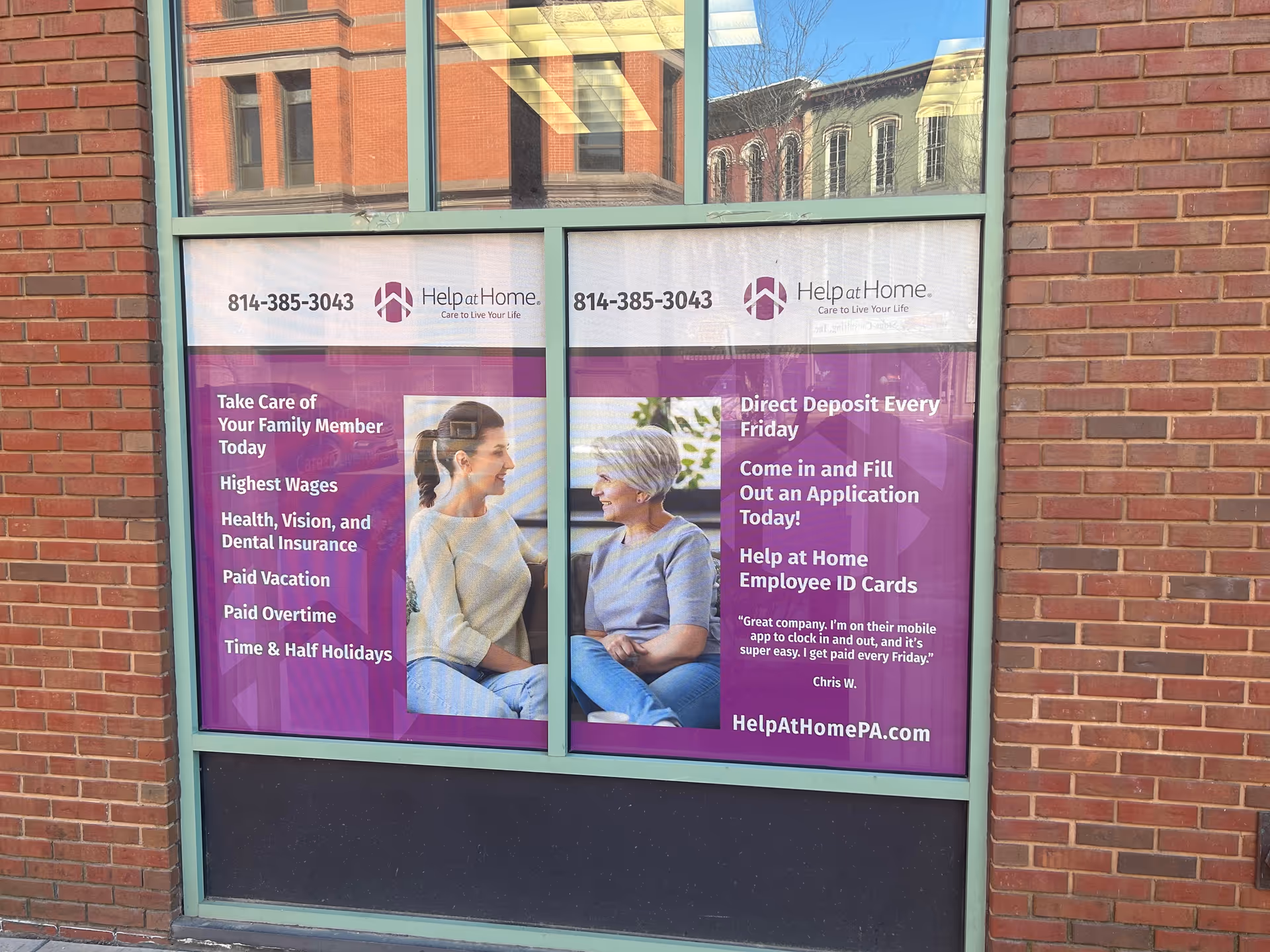 Brick building facade with two purple Help at Home window posters.