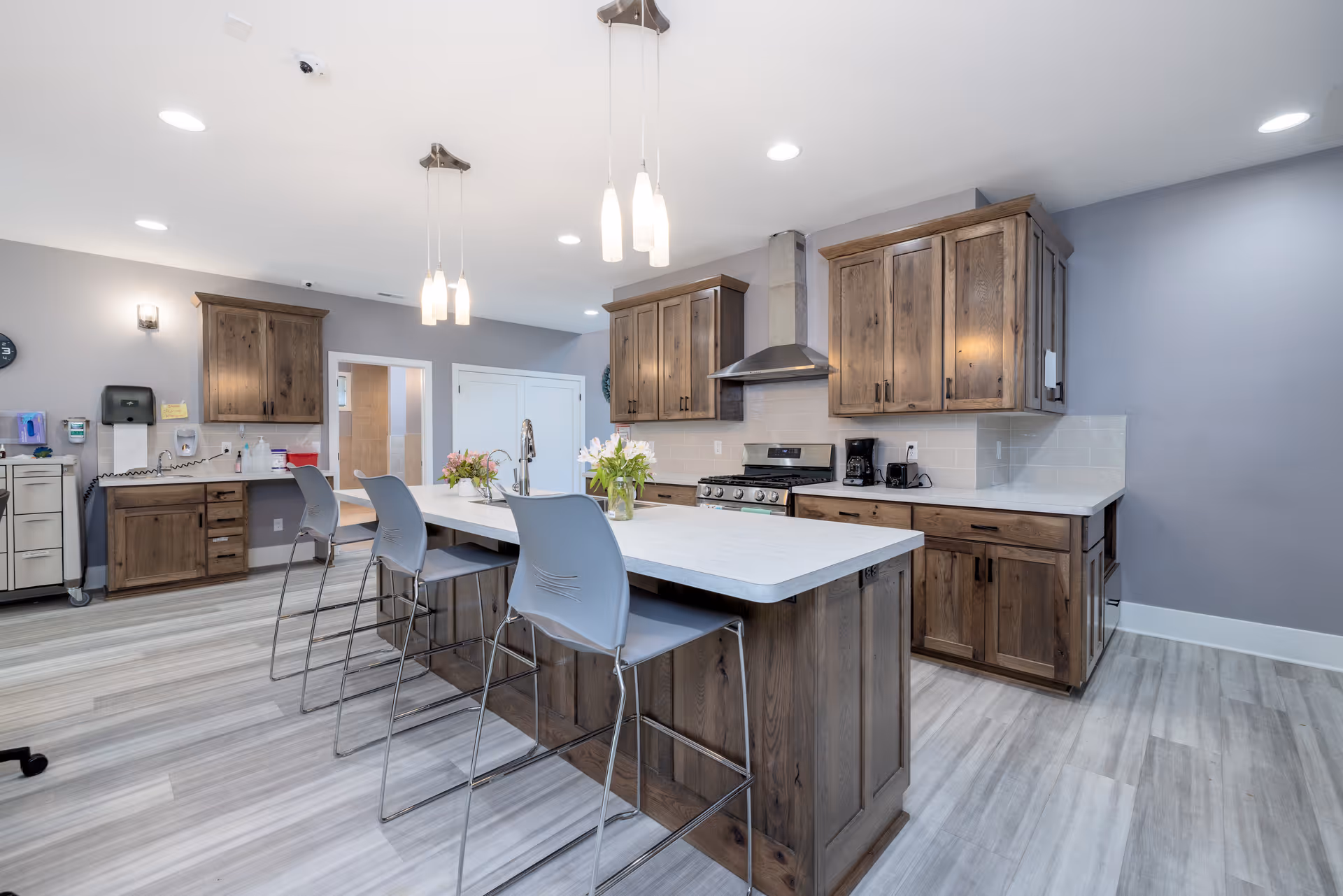 Modern communal kitchen with island, wooden cabinets, and bar stools in a senior facility.