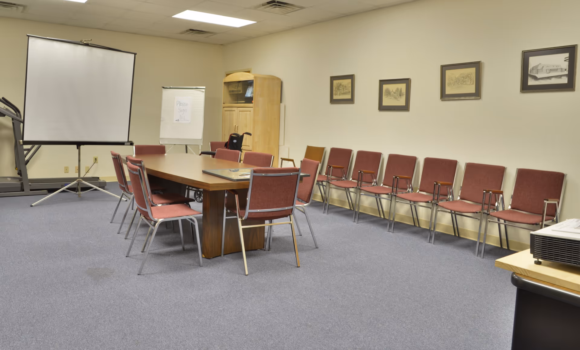 Long conference table in a meeting room with red chairs and a projector screen.
