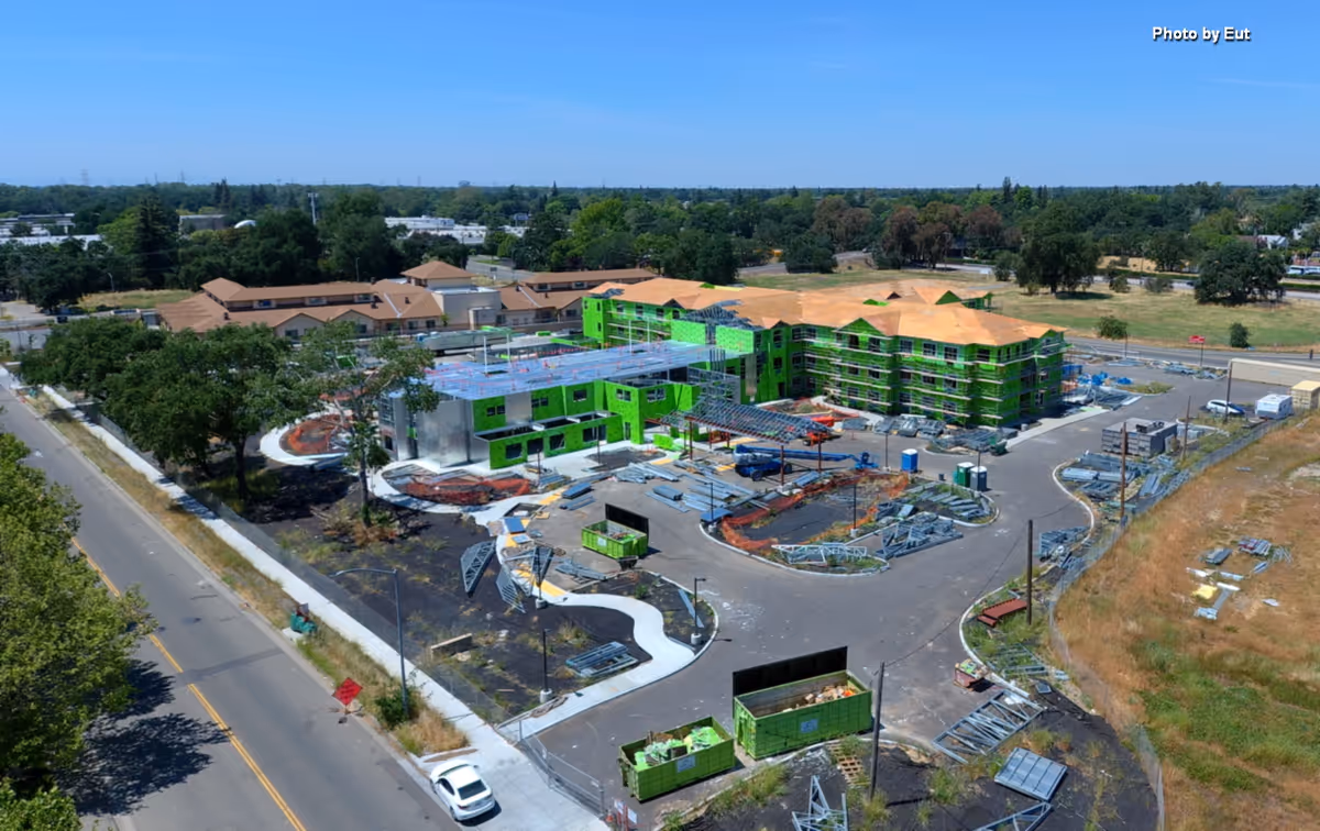 Aerial view of a building under construction with green exterior walls and surrounding site.