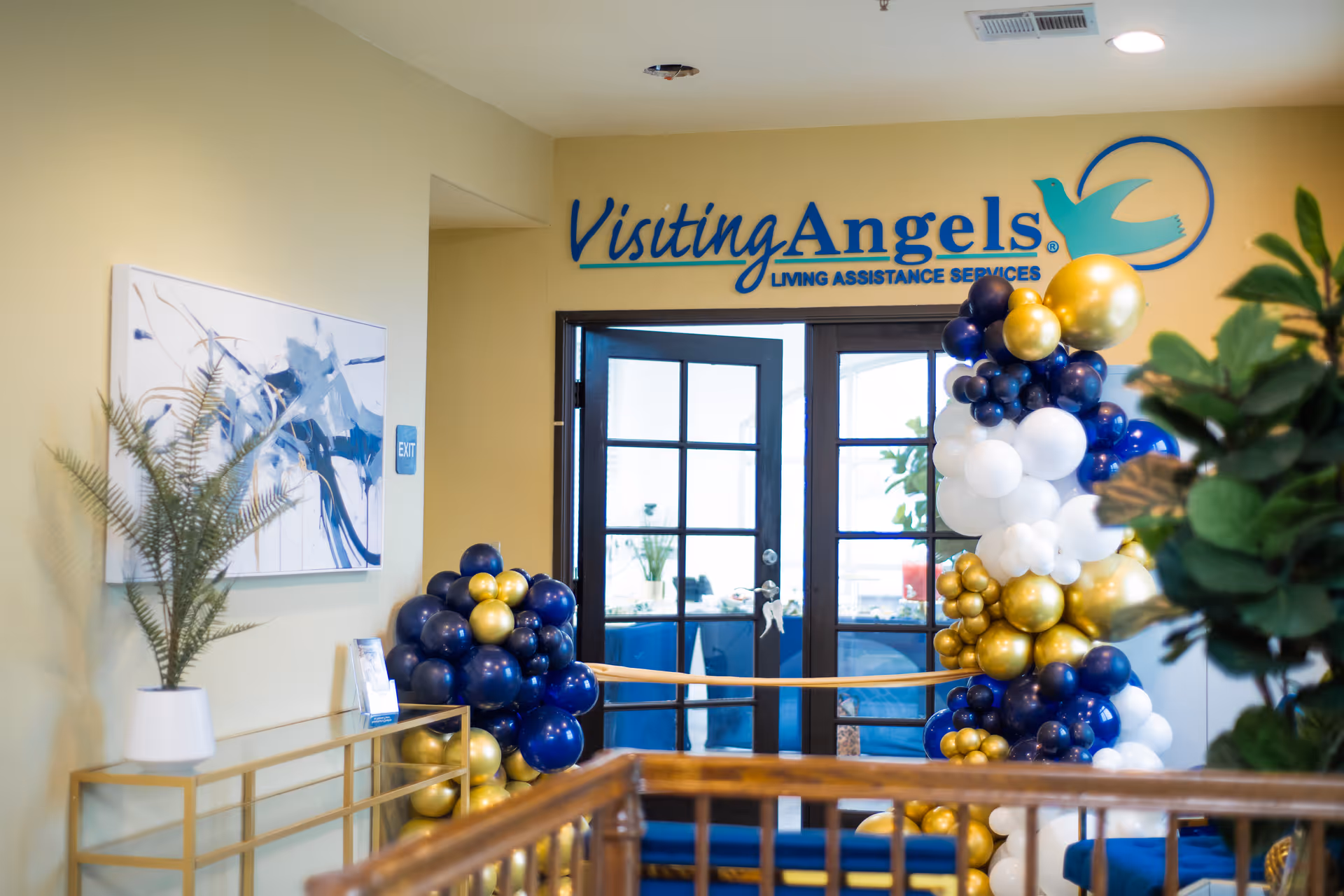 Interior lobby with Visiting Angels sign above double doors and blue and gold balloons.