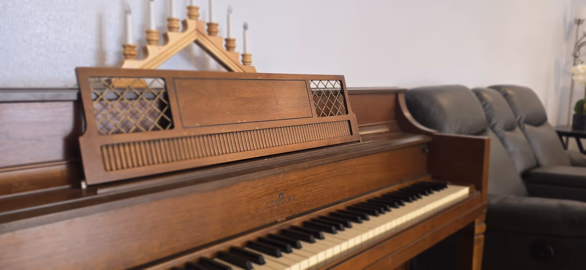 Wooden upright piano in a cozy living area with leather chairs.