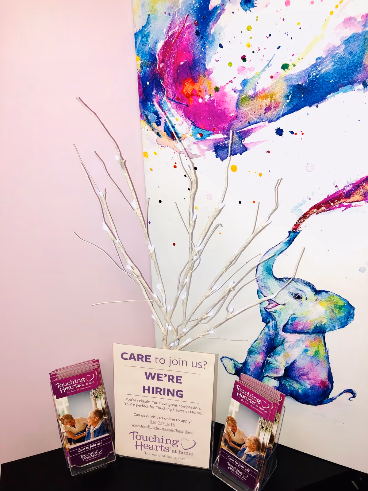 Indoor display area with colorful wall mural, elephant artwork, and hiring brochures near a pink wall.